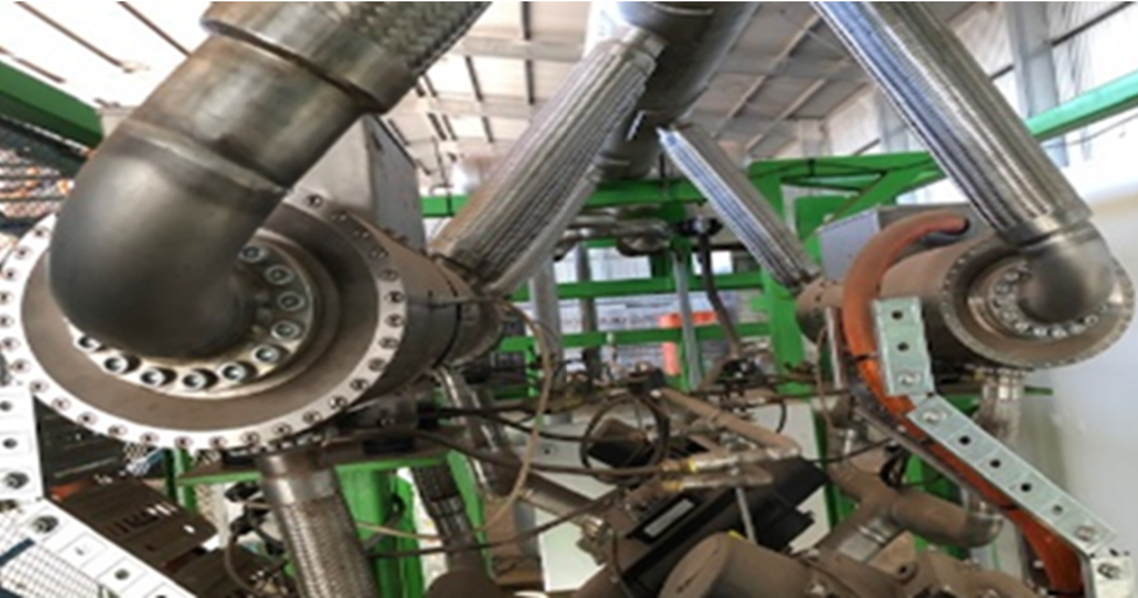Close-up of a large industrial robotic arm with multiple joints and bearings in a manufacturing setting, with a green metal framework in the background.
