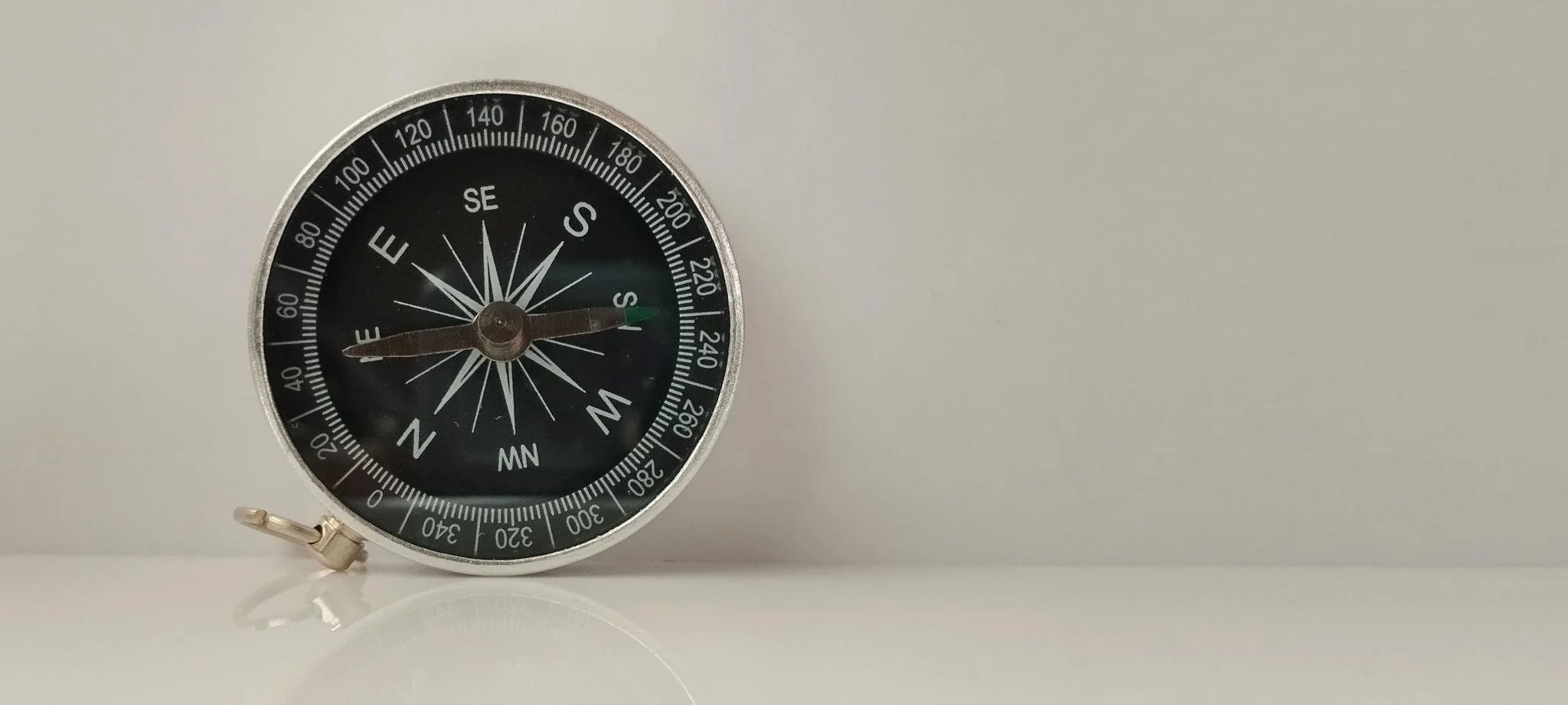 A black and silver compass with a glass face, resting on a white surface against a plain white background.