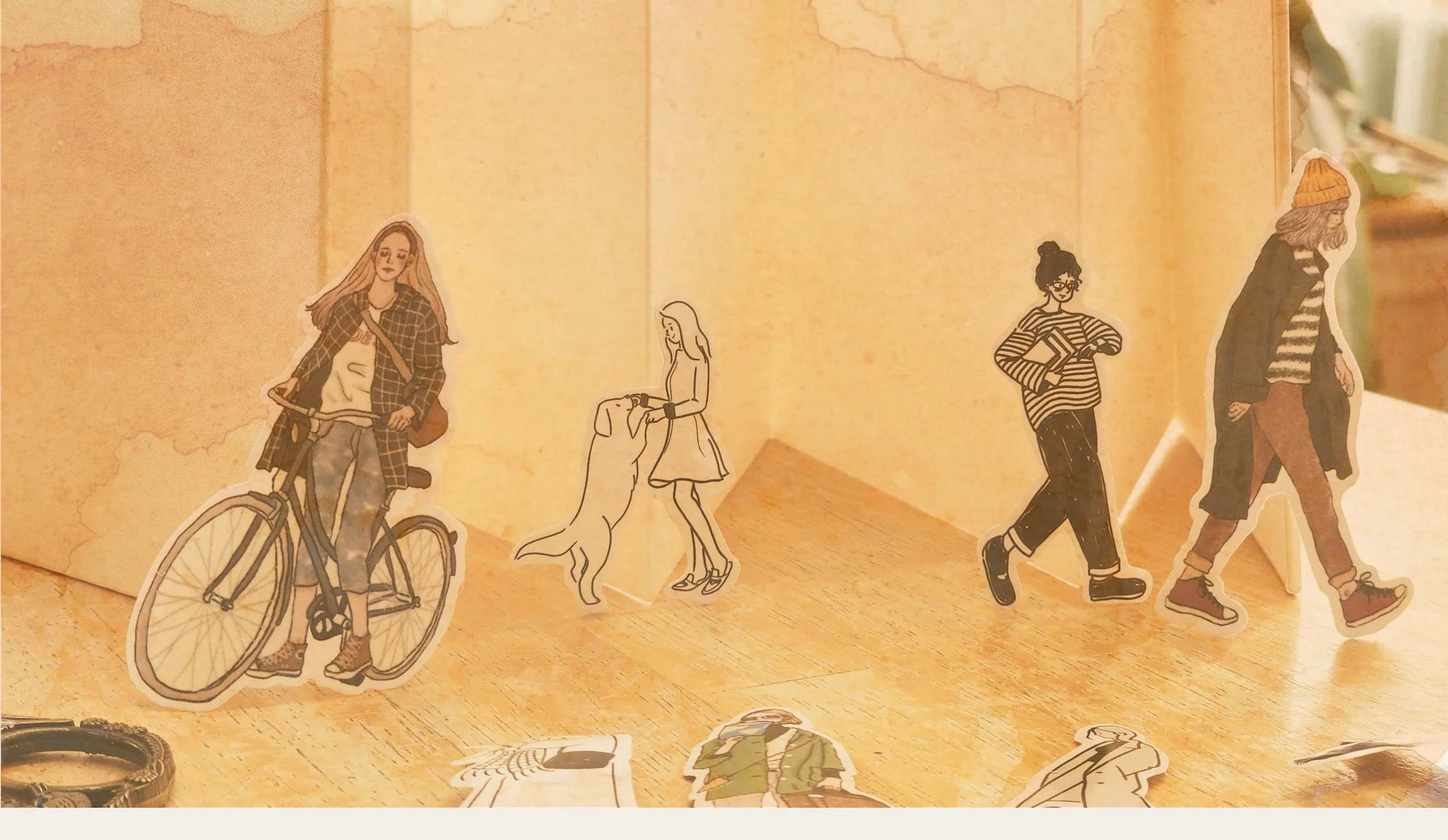 Découpes en papier représentant des femmes en marche ou à vélo, disposées sur une surface en bois. L'arrière-plan est de couleur beige pâle.