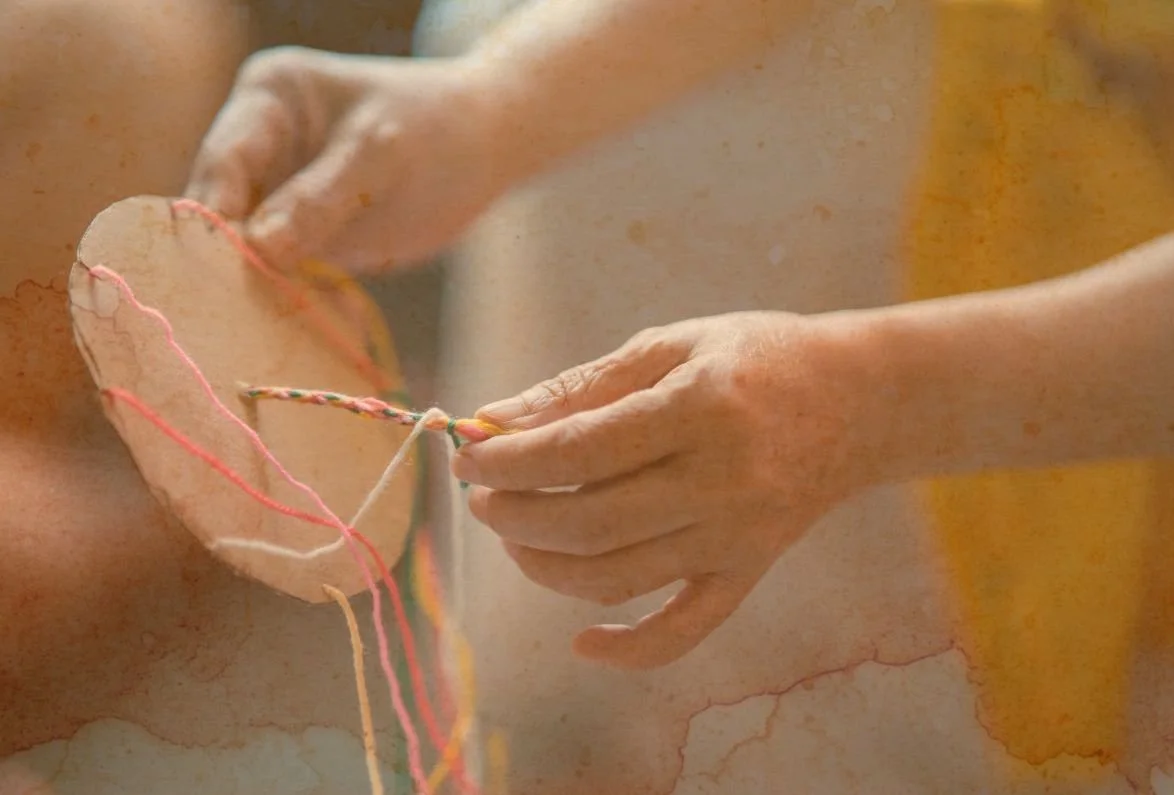 Une personne qui fait une création avec des fils colorés à travers un morceau de carton.