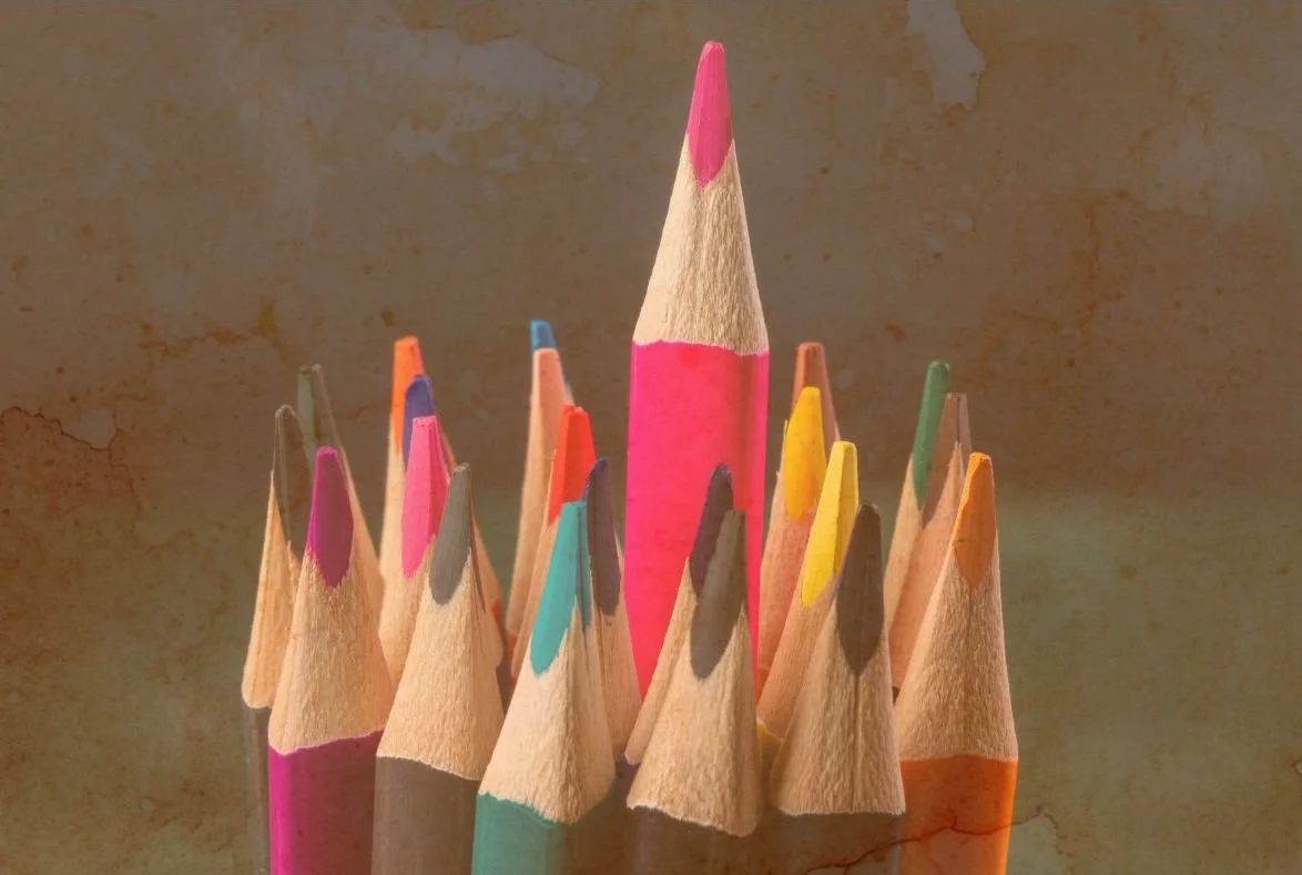 Un groupe de crayons de couleur, dont un au centre de couleur rose, entourés d'autres crayons de différentes couleurs, tous pointus.