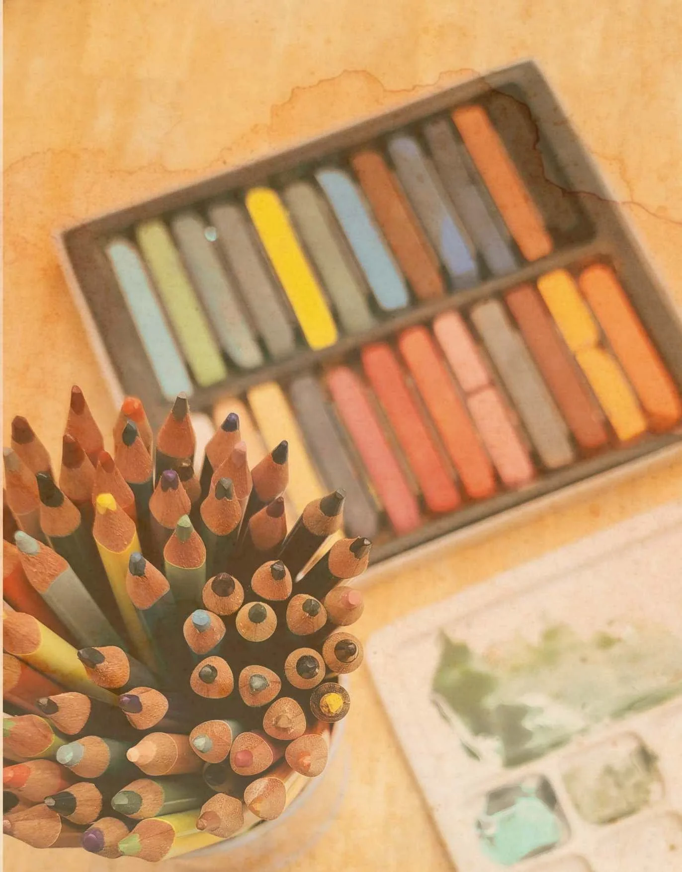 Un pot de crayons de couleur, un boîtier de pastels et une palette de peintures sur une surface en bois.