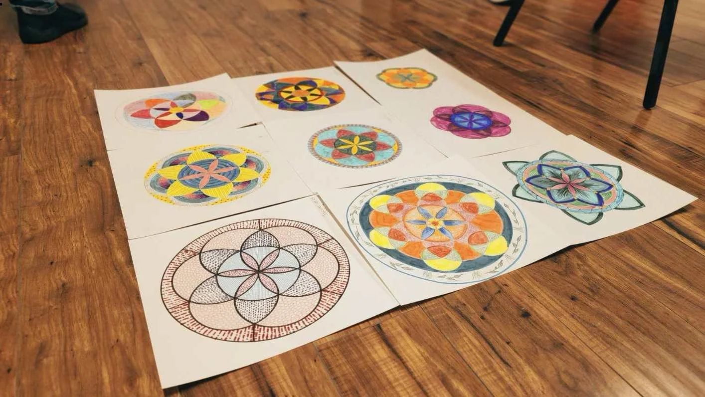 Divers dessins de mandalas colorés et géométriques étalés sur un sol en bois.
