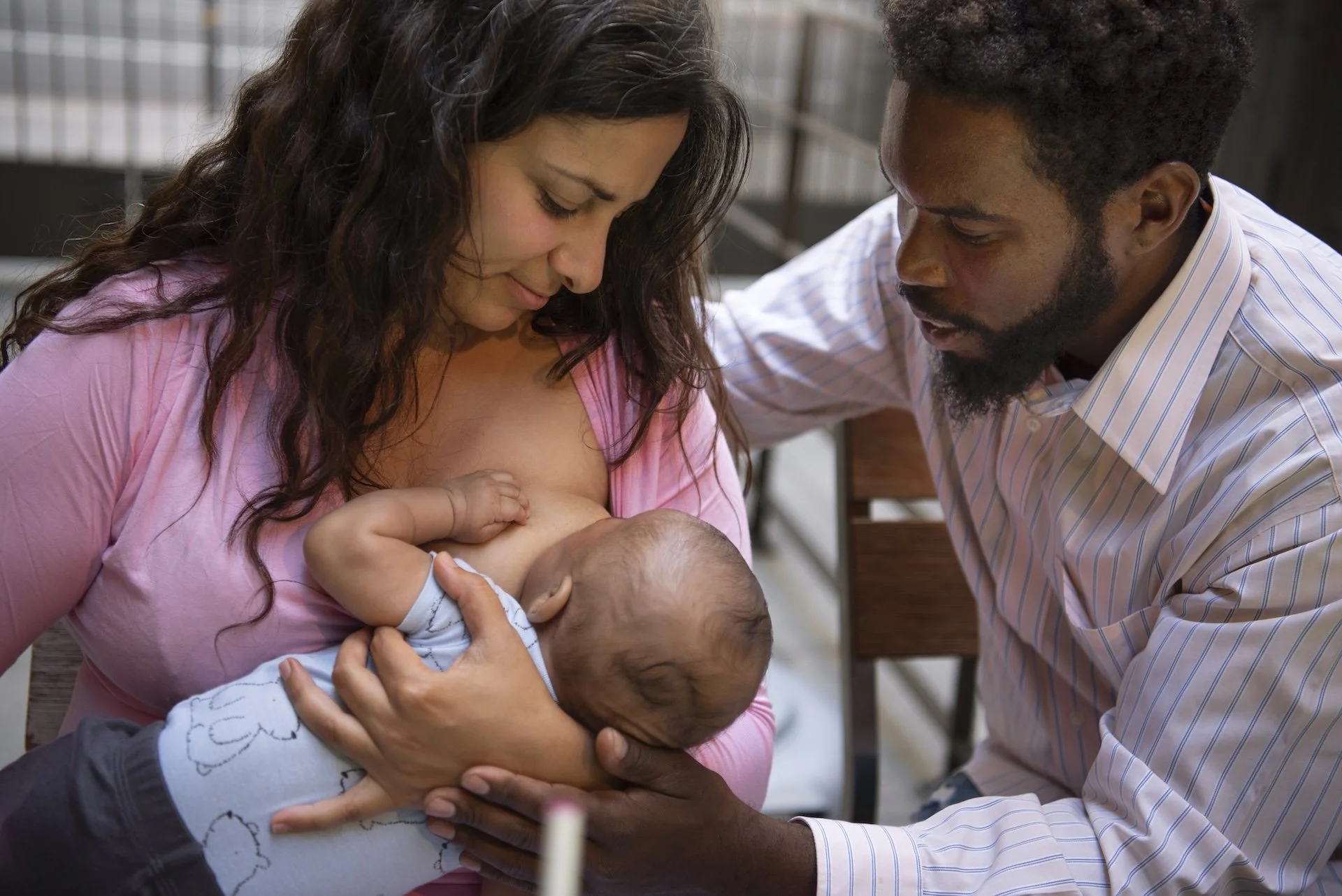 A woman breastfeeding a baby while a man looks on with affection.