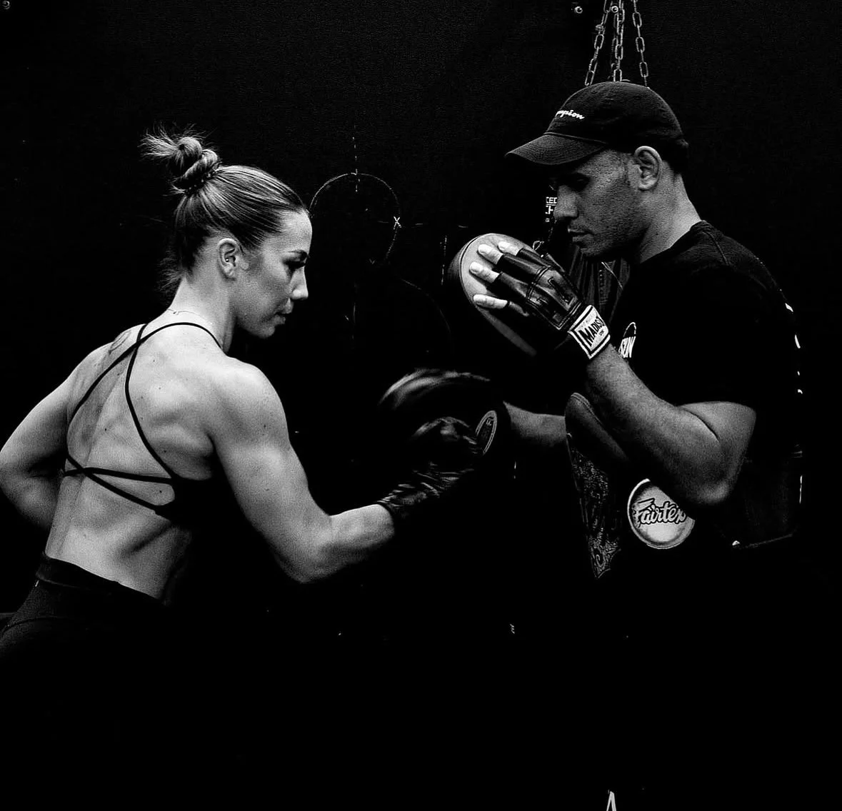 A woman boxing training with a trainer in a gym, both in boxing gloves, with the woman receiving guidance from the trainer during her workout.