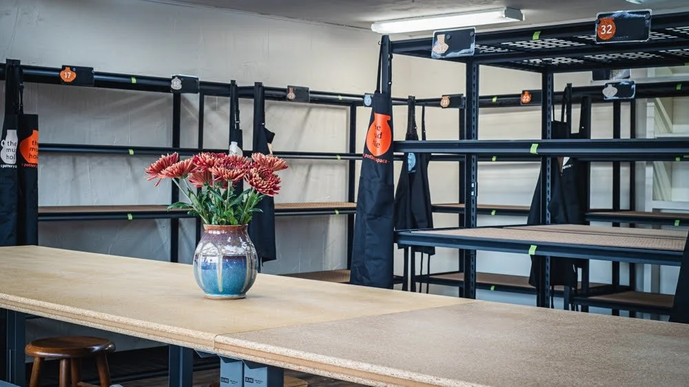 Empty black metal shelving units in a room with a wooden table and a glass vase of pink flowers.