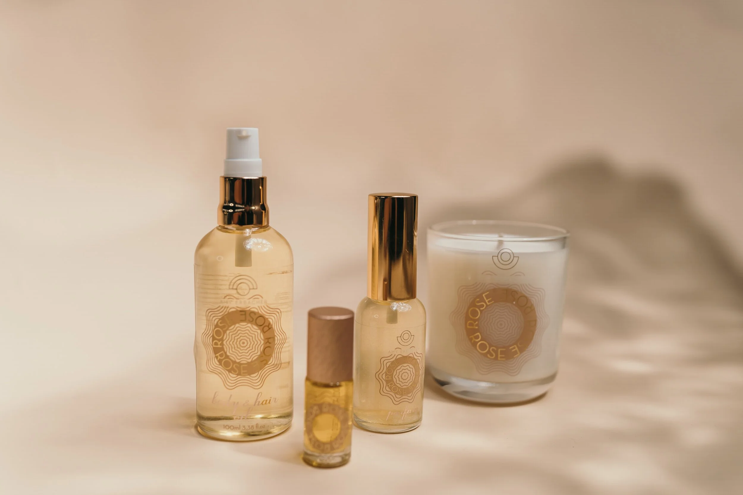 Beauty products including spray bottles and jars with gold accents and labels on a white surface.