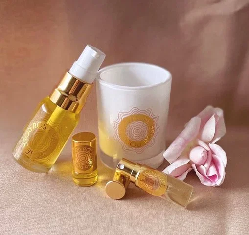 Skincare products with gold accents, a white candle in a white container, pink roses, and a beige background.