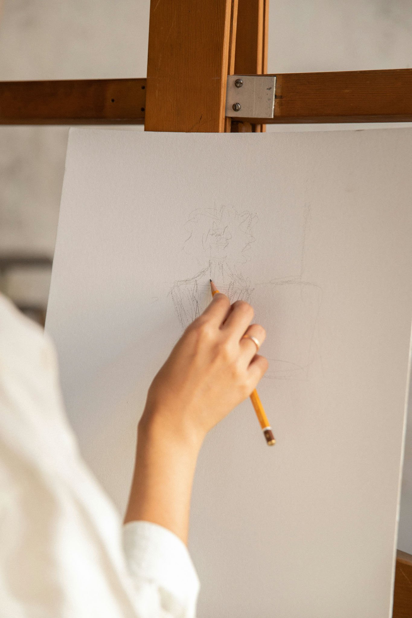 A person sketching a portrait on a white piece of paper with a pencil, viewed from the side, with a wooden structure in the background.