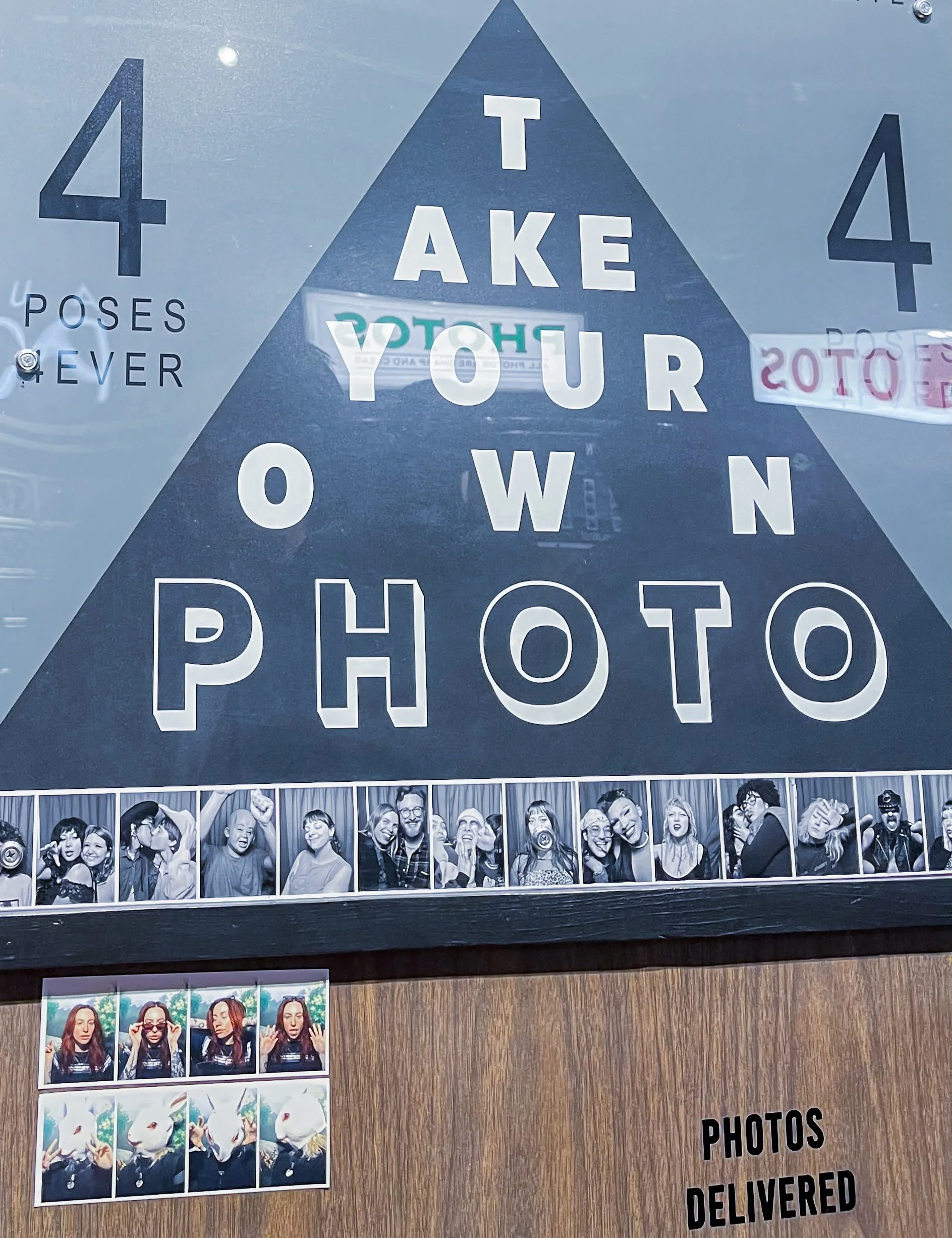 Sign reading “take your own photo” next to a photobooth with sample photo strips displayed.