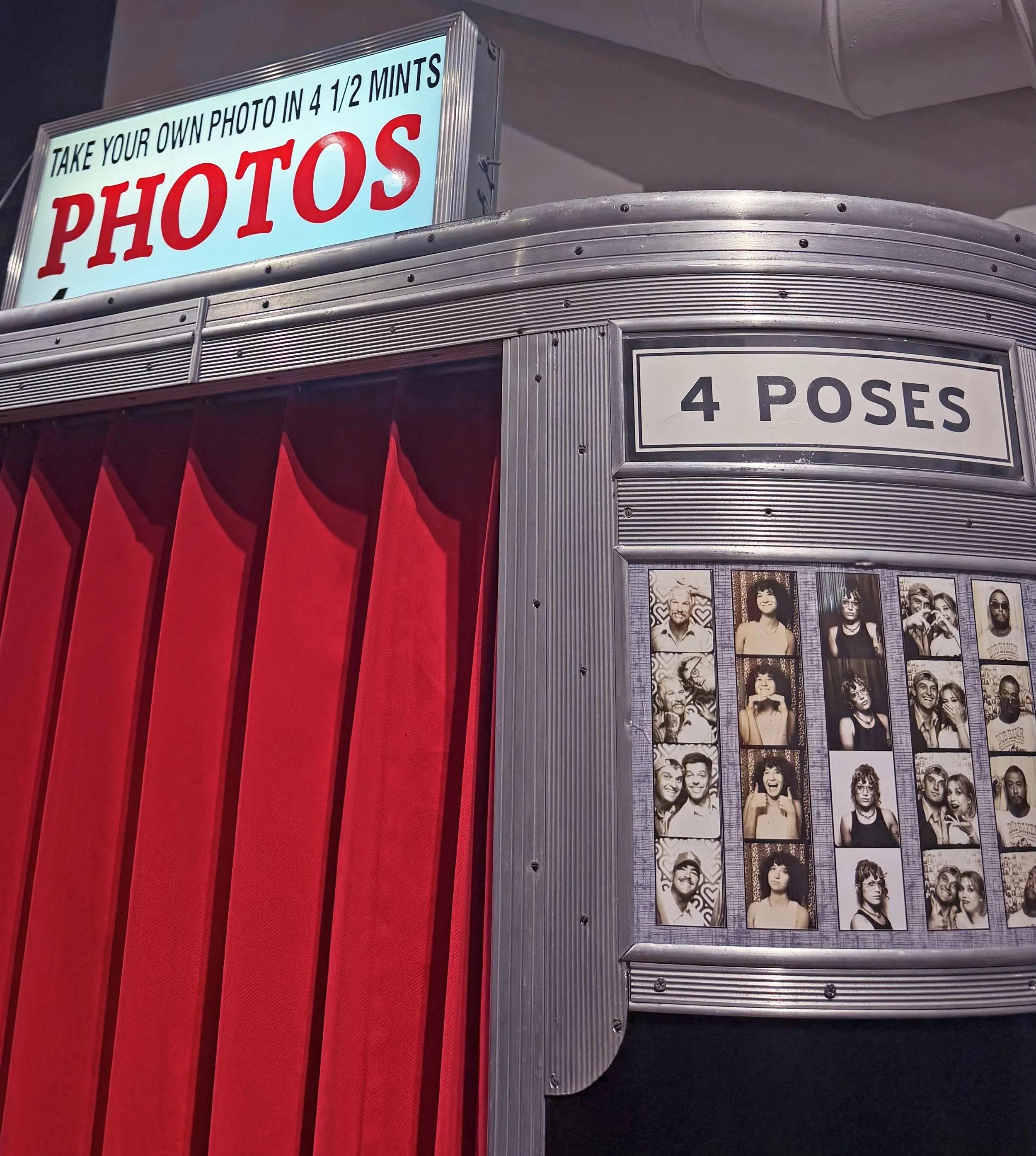 Photobooth with red curtain and sign reading “4 poses” inside the studio.