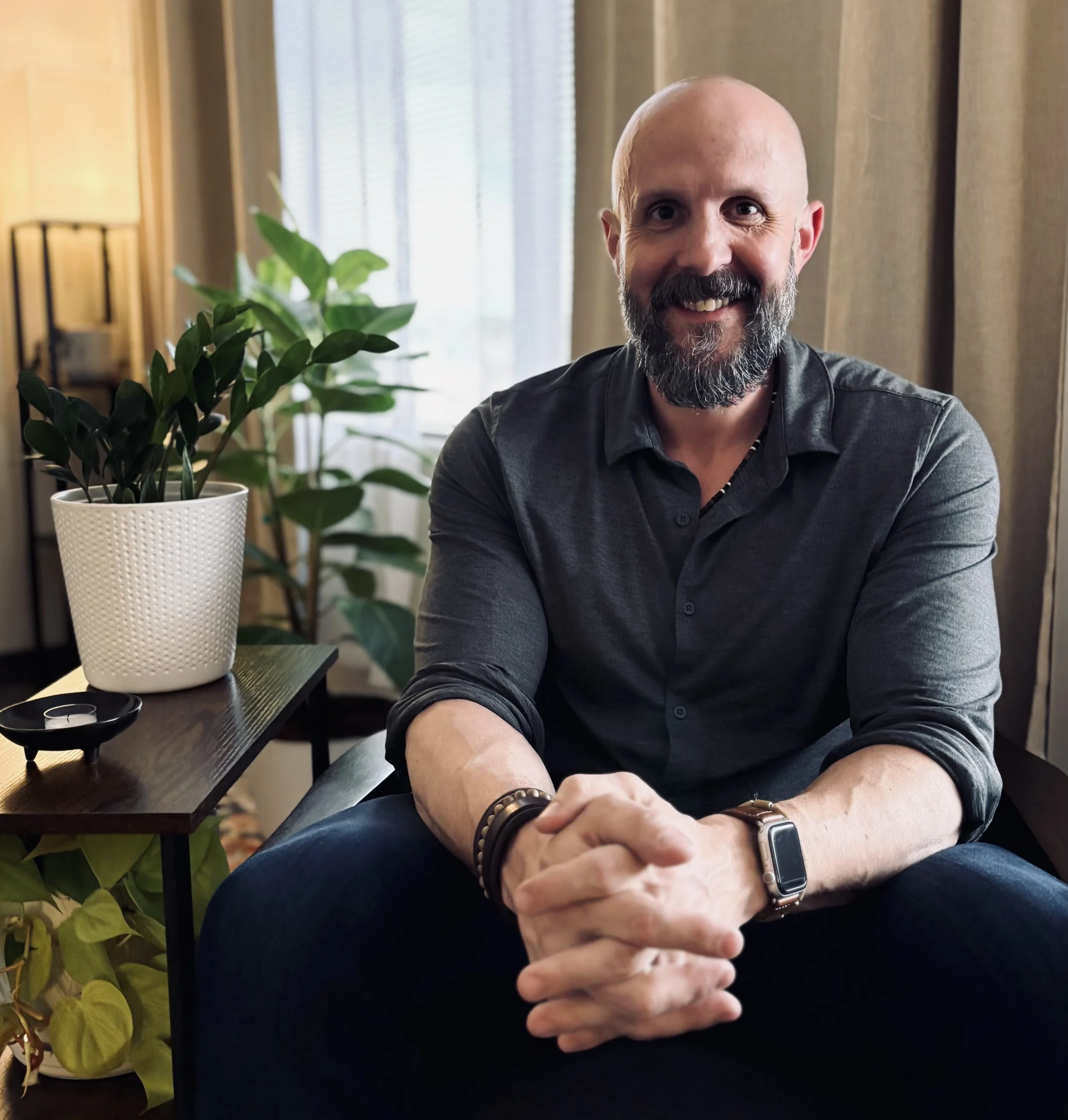 Smiling male, in pleasant Denver office, with green plants and a wooden table