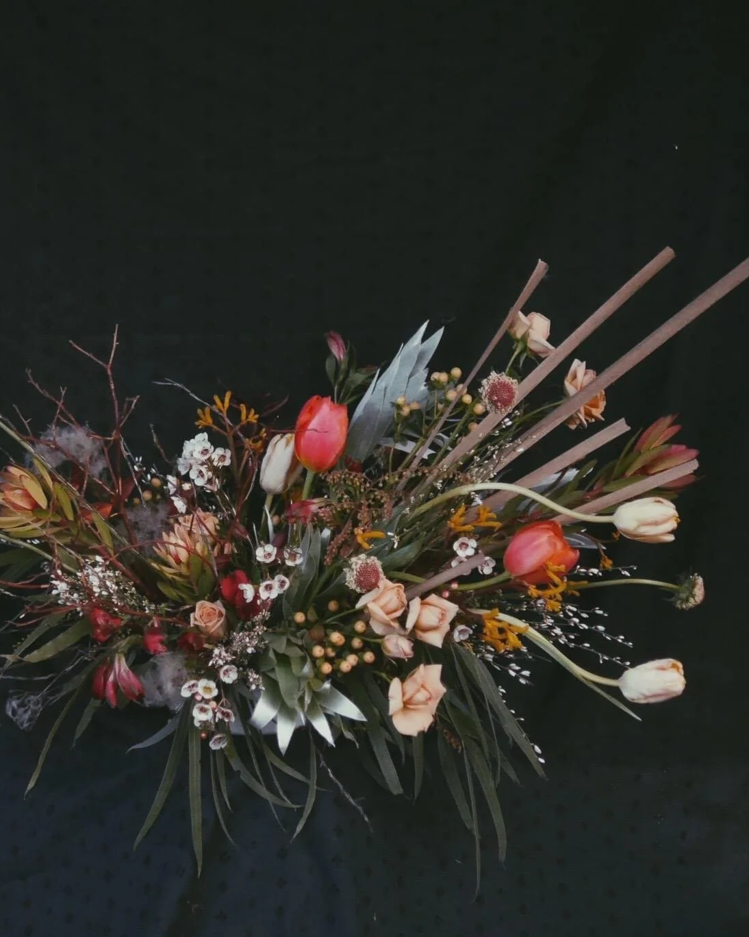 A floral arrangement with tulips, roses, and various greenery on a black background.