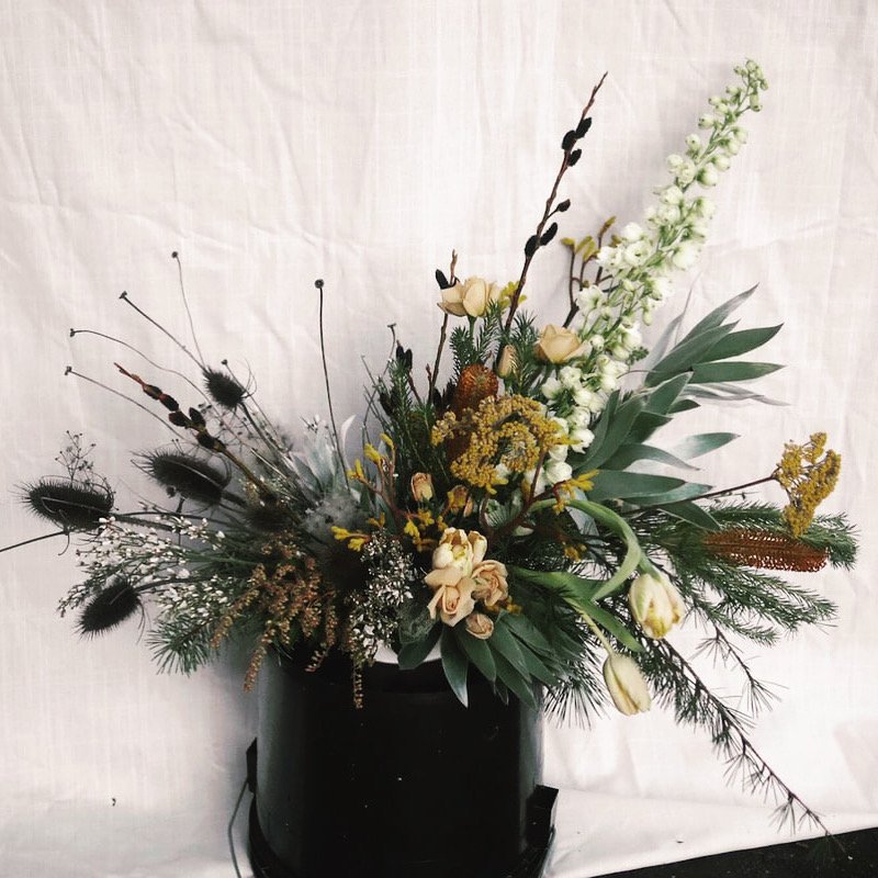 Arrangement of white, cream, and yellow flowers with green foliage in a black vase against a white background.