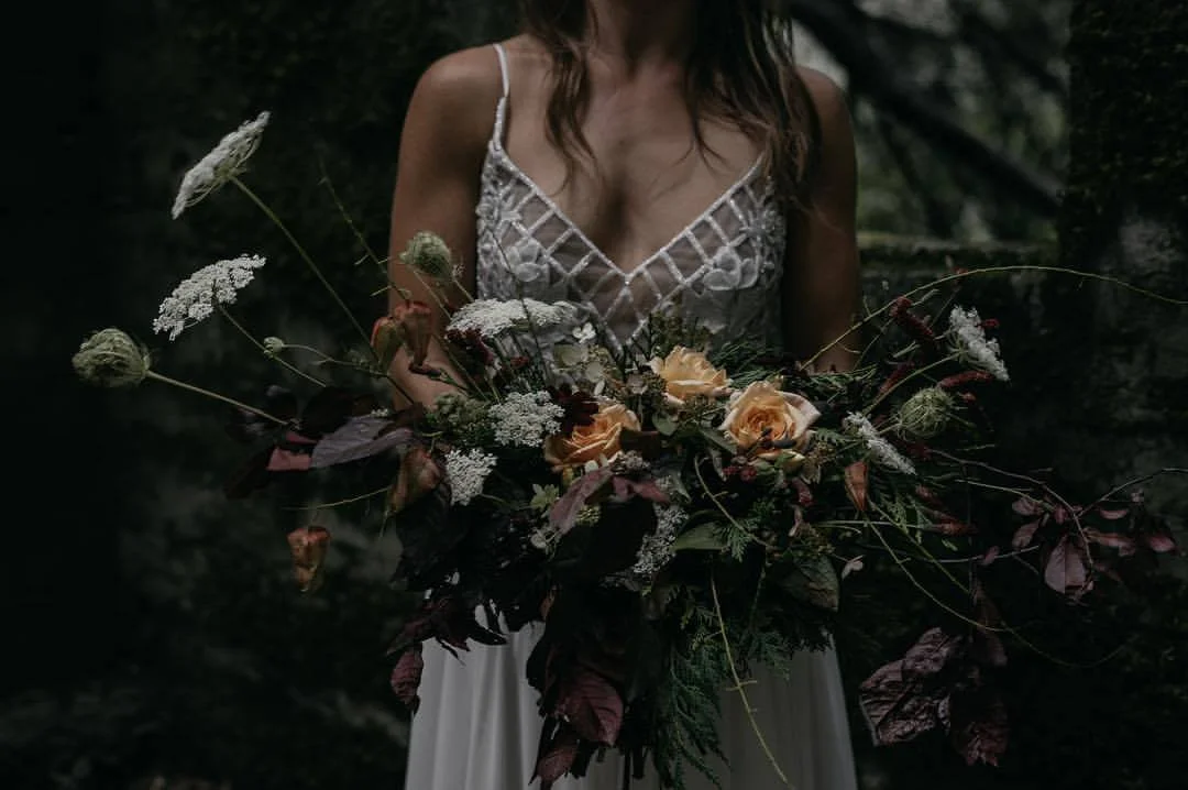 Woman in a white dress holding a large bouquet of flowers in a dark outdoor setting.