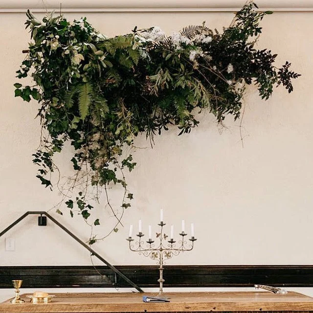 Decorative greenery arrangement hanging above a wooden table with a gold candelabrum and some small items.