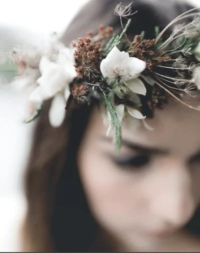 Close-up of a young woman wearing a floral crown with white and brown flowers and greenery.