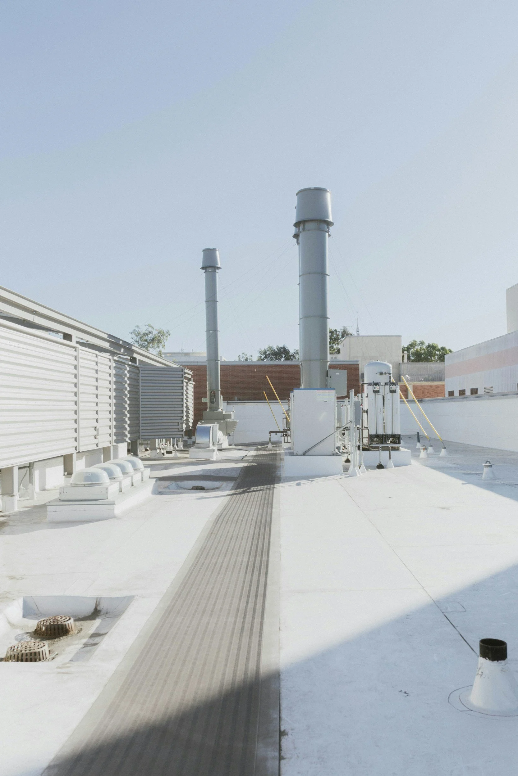 Rooftop with two large exhaust pipes, various vents, and electrical boxes under a clear sky.