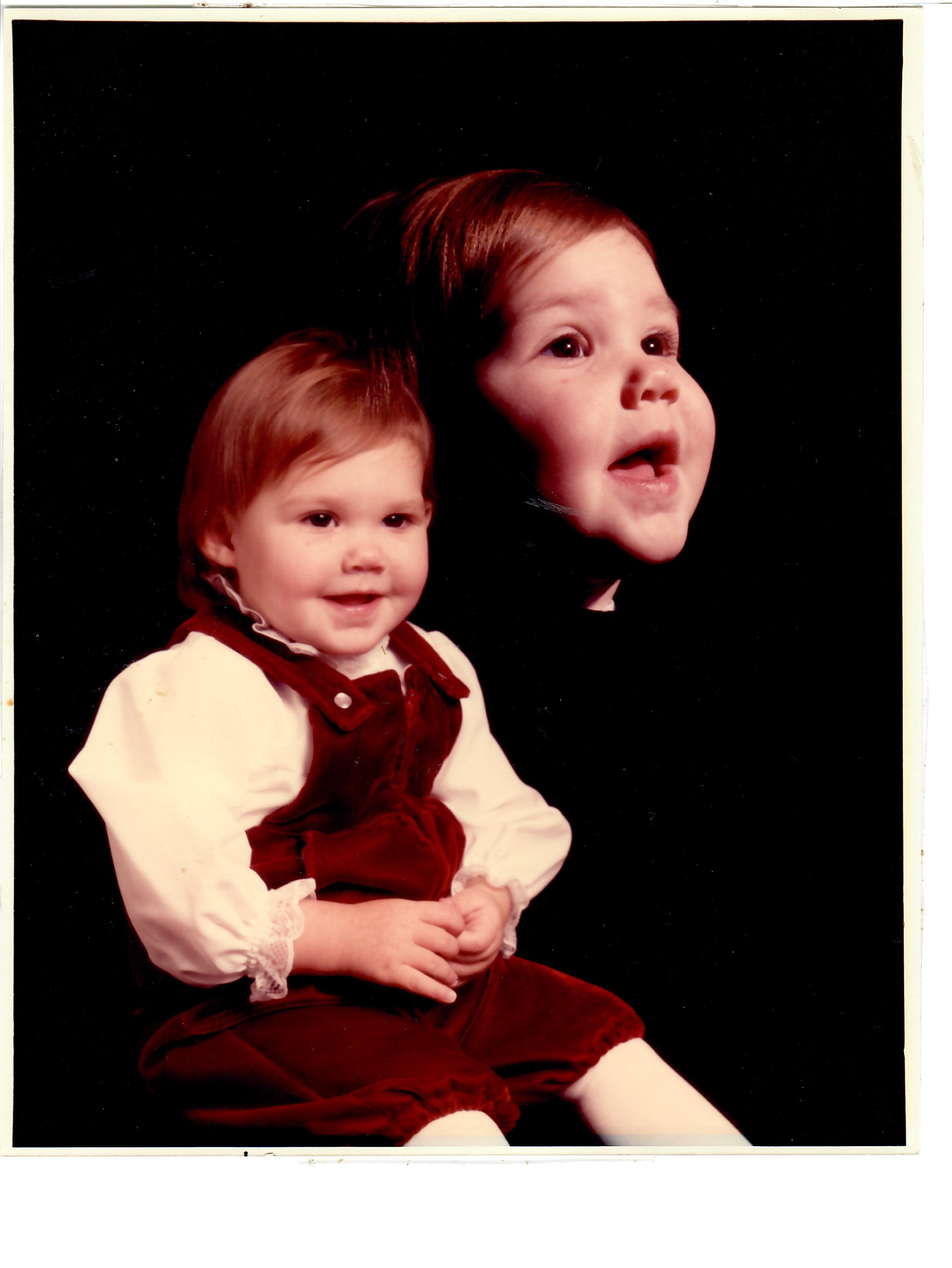Two young children, a girl and a boy, dressed in Christmas costumes with a black background.