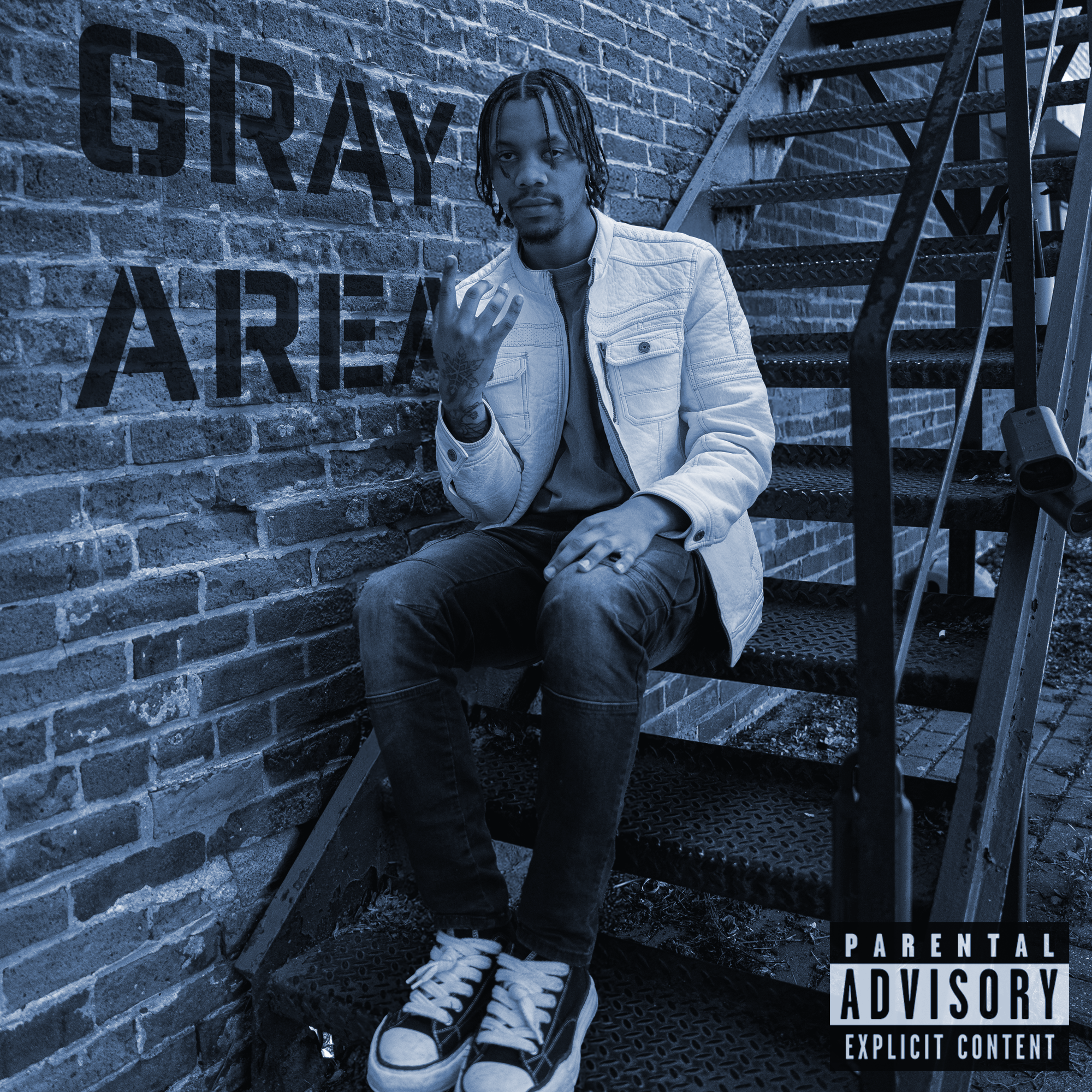 A young man sitting on metal stairs next to a brick wall with a painted sign that reads 'GRAY AREA.' He has dreadlocks, tattoos on his left hand, is wearing a light-colored jacket, dark jeans, and sneakers, and is holding up his middle finger. There is a 'Parental Advisory' warning label at the bottom right corner.
