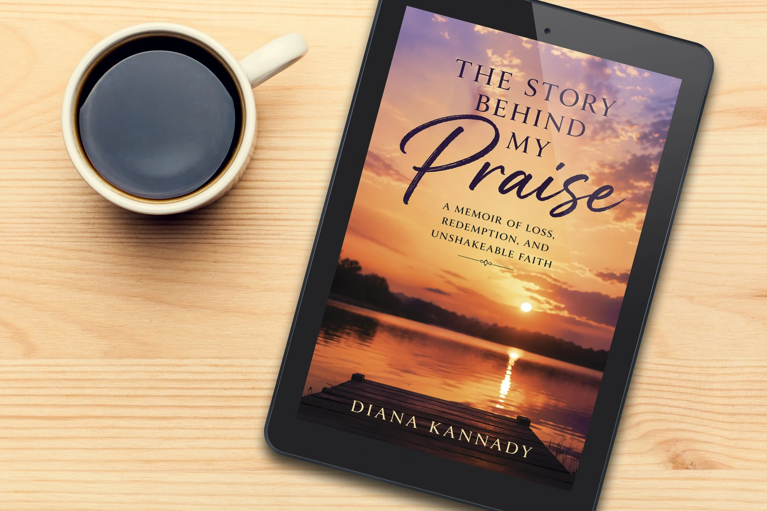 A cup of black coffee next to an e-reader displaying the cover of a book titled "The Story Behind My Praise" by Diana Kannady, with a sunset over a lake in the background.