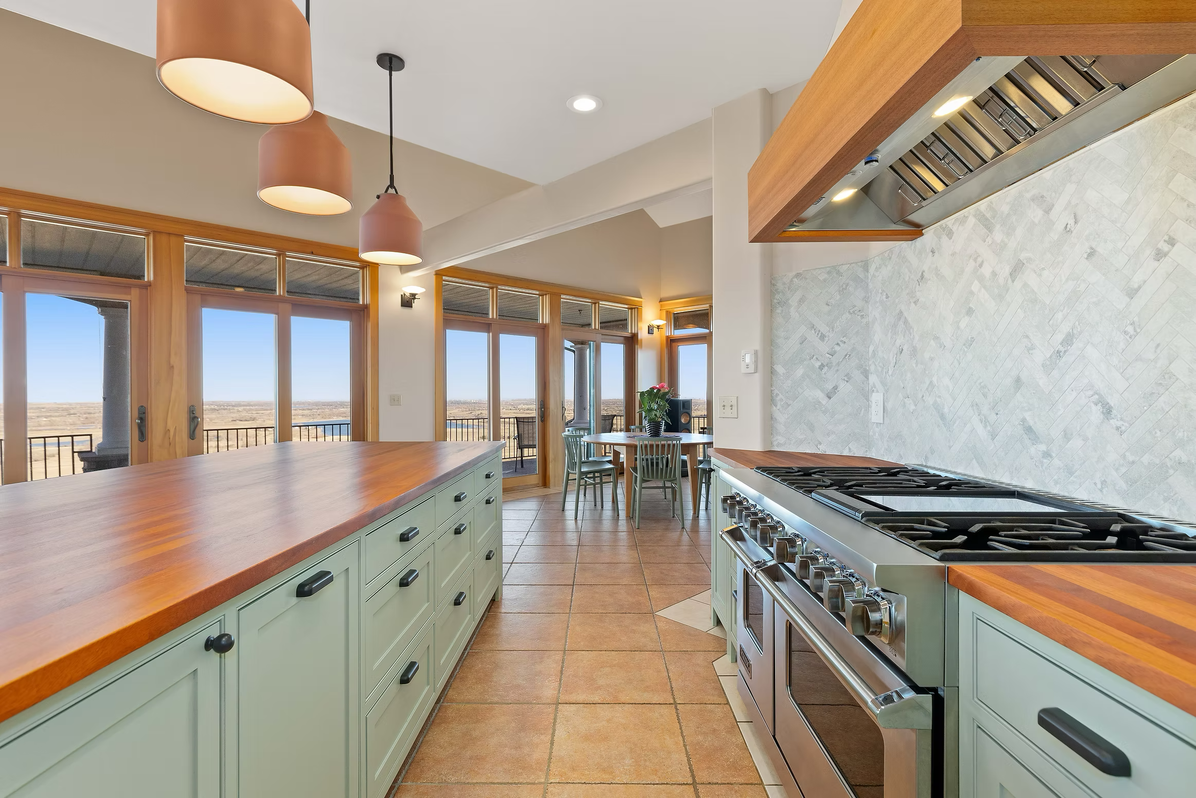Kitchen with light green cabinets, wooden countertops, a stainless steel stove, and large windows with views of a landscape.
