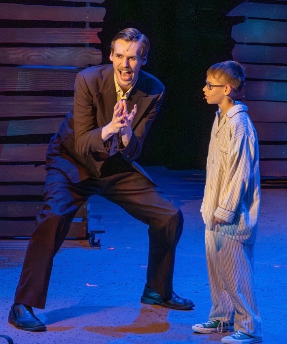 Aidan Ryan, a young actor with blonde hair and a mustache, on stage during a performance