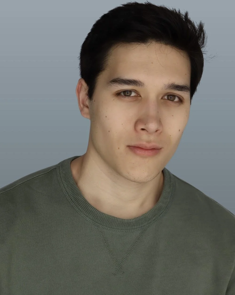 Liam Henry Pham, a young actor with dark brown hair and brown eyes, in a green shirt against a light blue gray backdrop