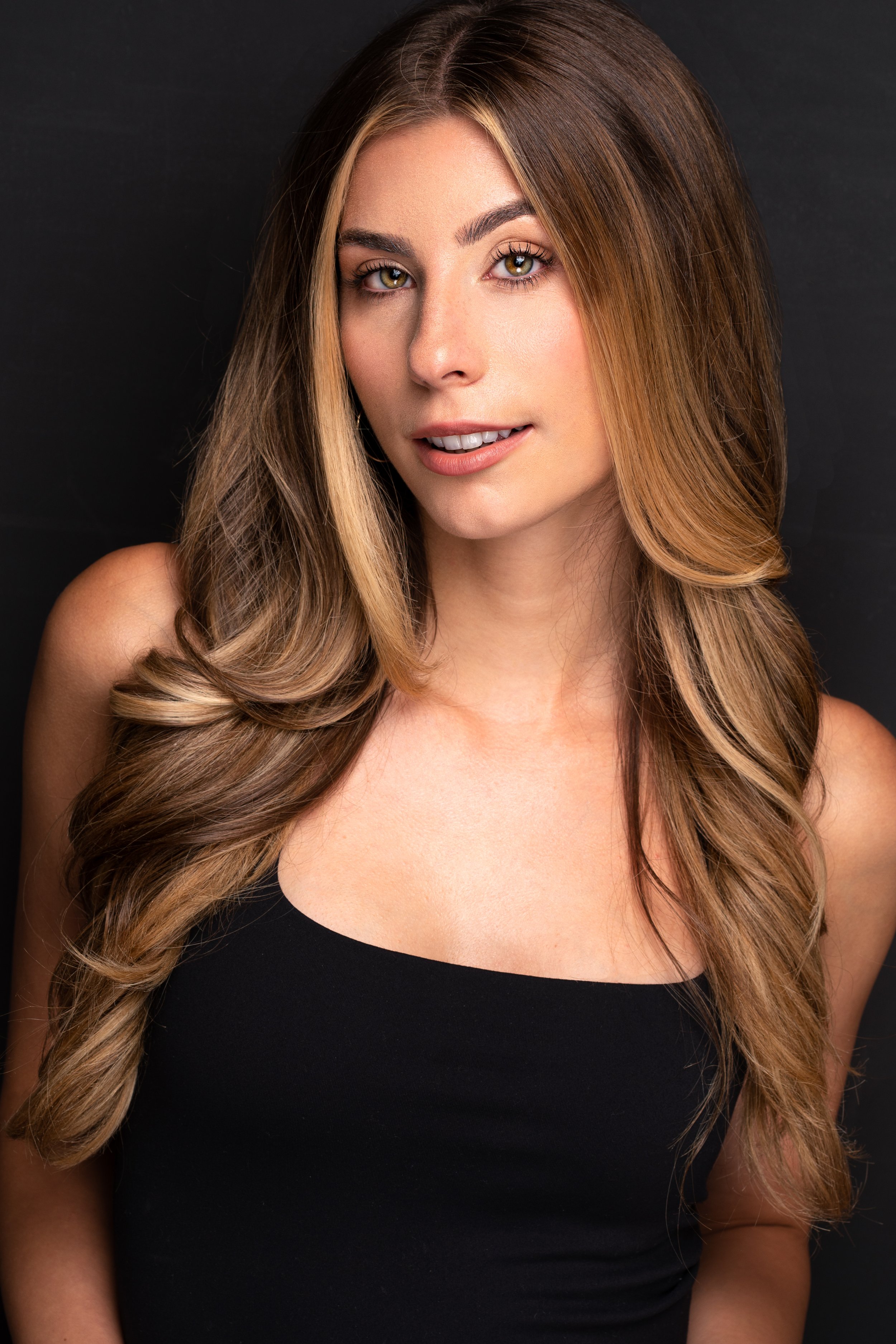Alex Hope Donach, a young actress with highlighted brown hair and brown eyes, in a black tank top against a gray backdrop