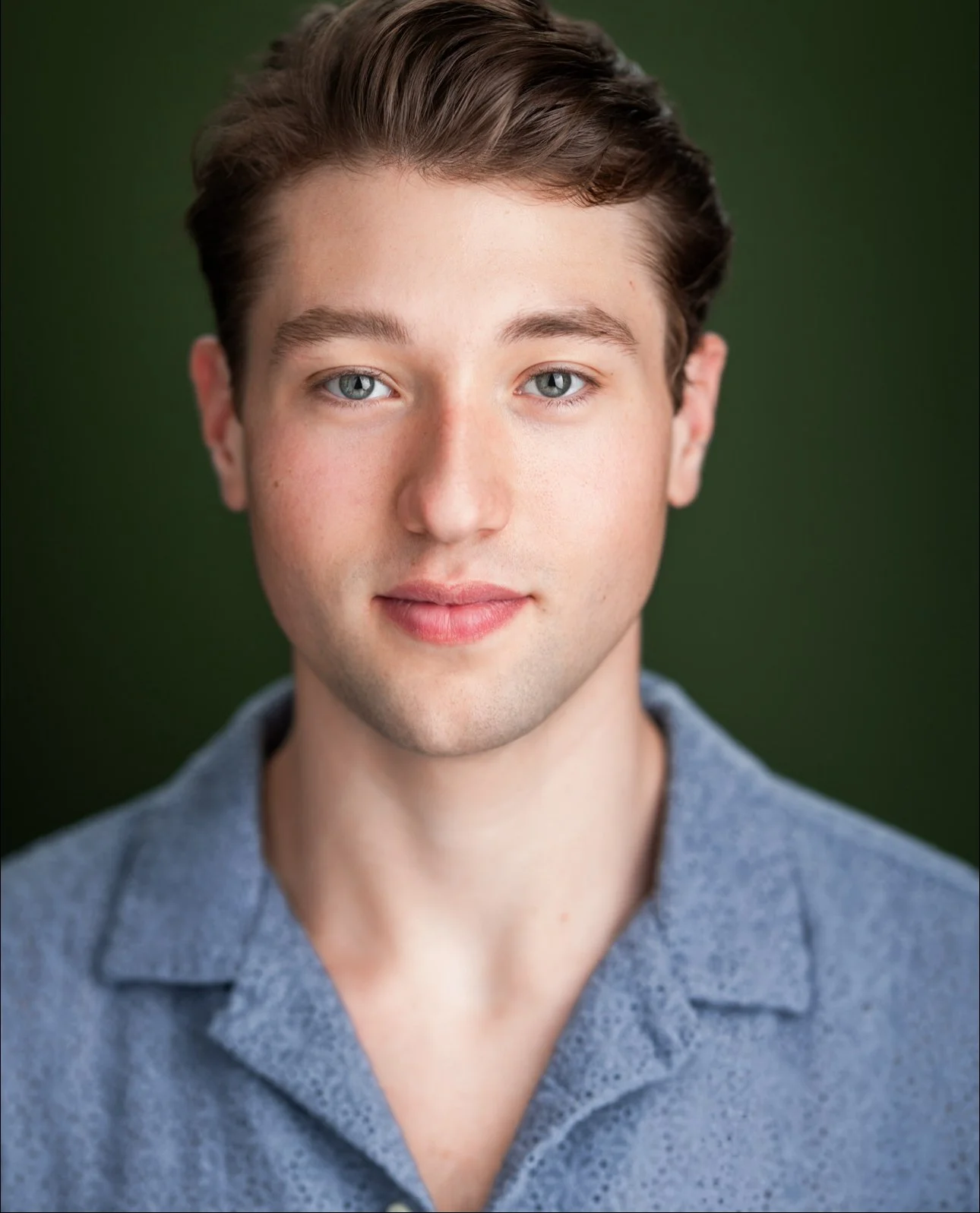 Jack Plogger, a young actor with brown hair and green eyes, in a light blue polo shirt against a green backdrop