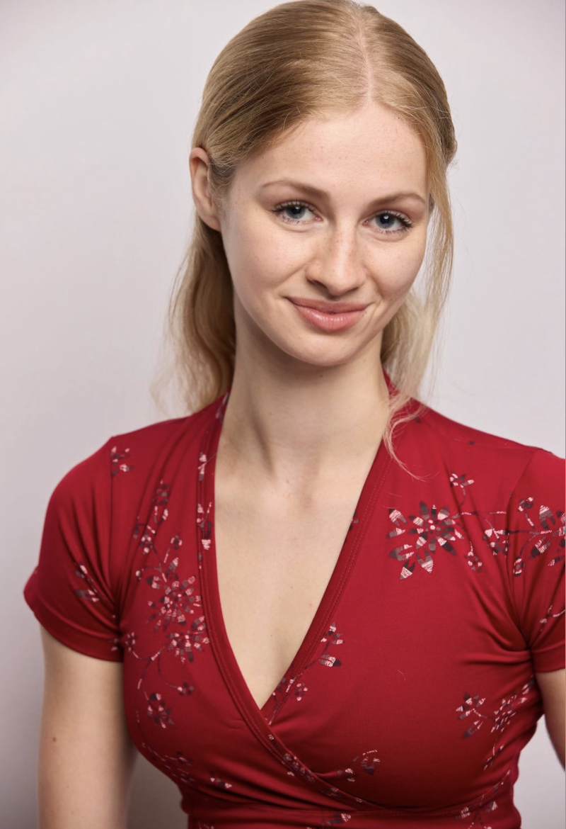 Annie Thomas, a young actress with blonde hair and blue eyes wearing a red floral dress against a white backdrop