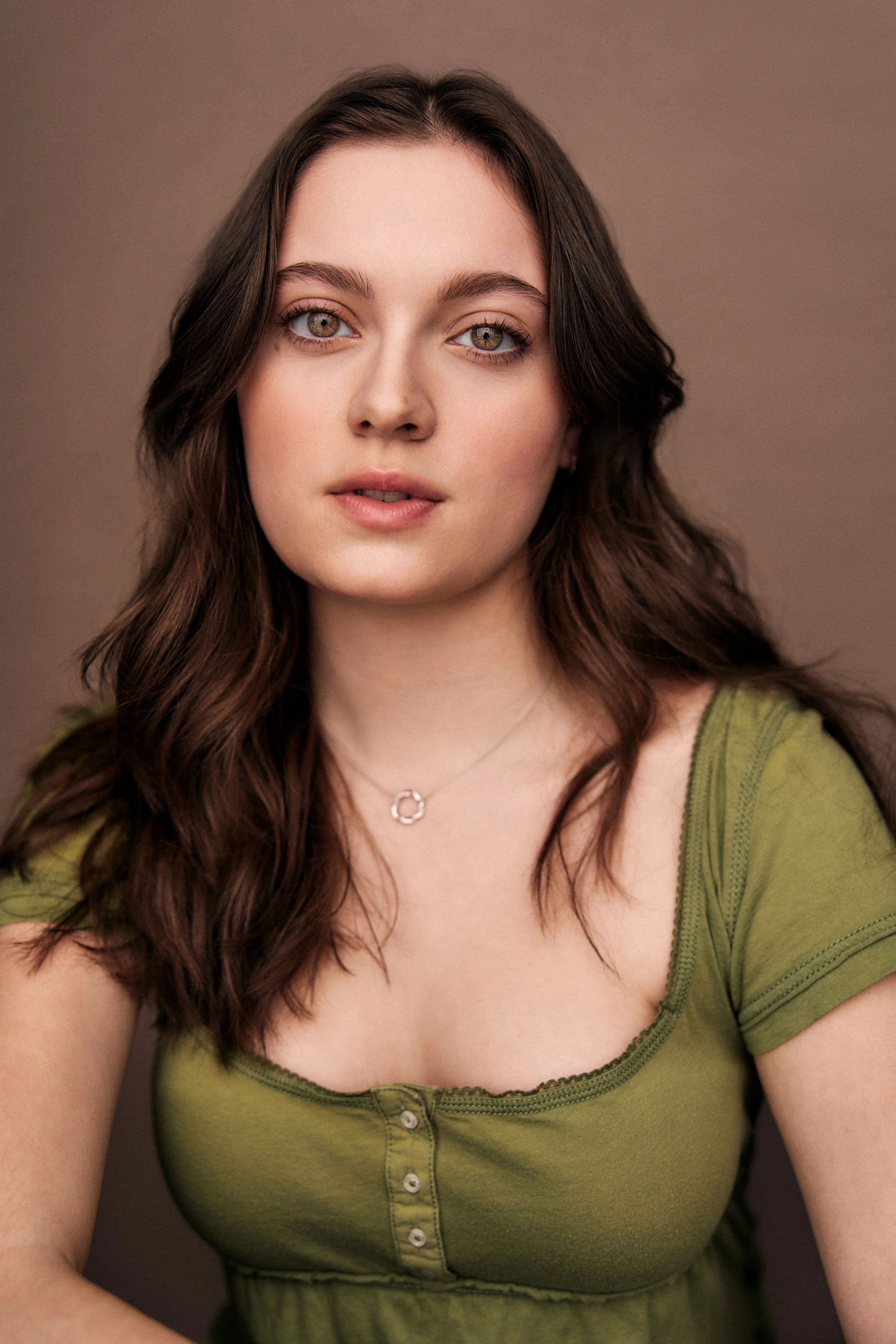 Carolyn Dunbar, a young actress with wavy brown hair and brown eyes, in a green top against a brown backdrop