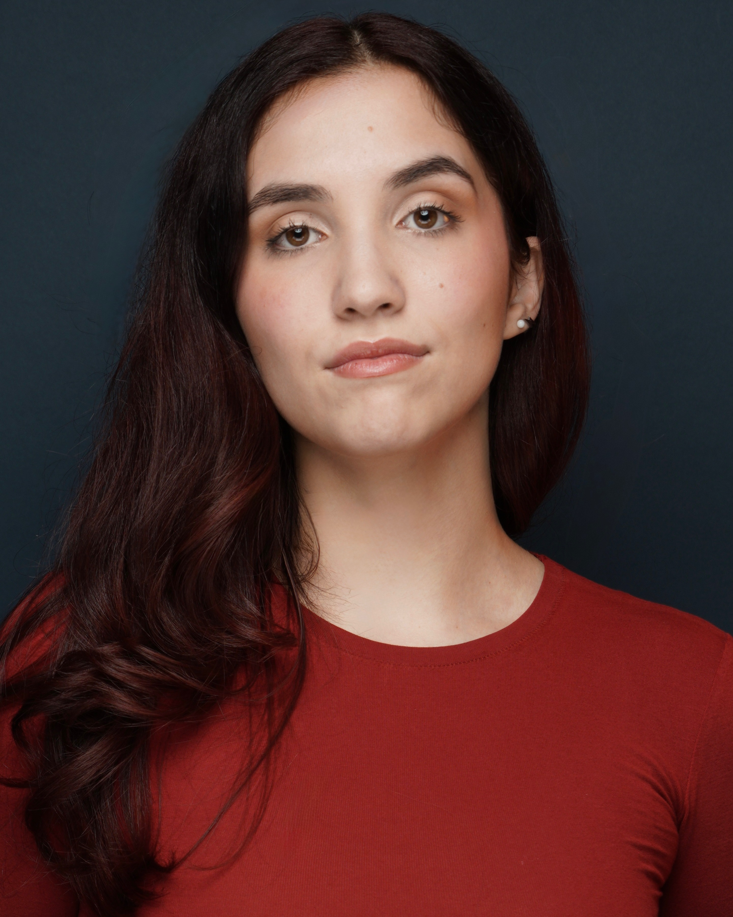 Andrea Mongil, a young actress with dark red hair and brown eyes, in a red top against a dark blue backdrop