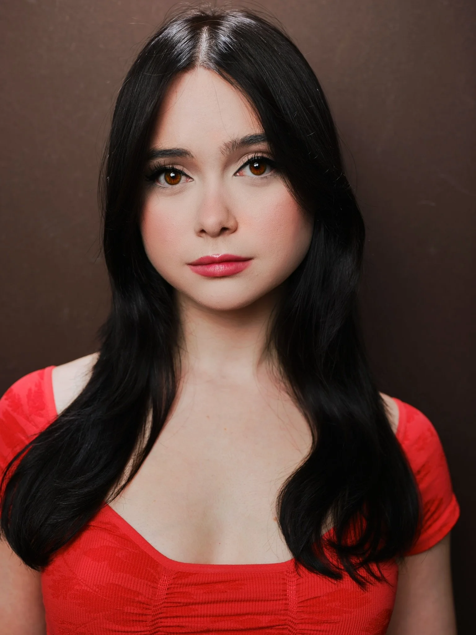 Margot May Waldron, a young actress with dark brown hair and brown eyes, in a red top against a brown backdrop