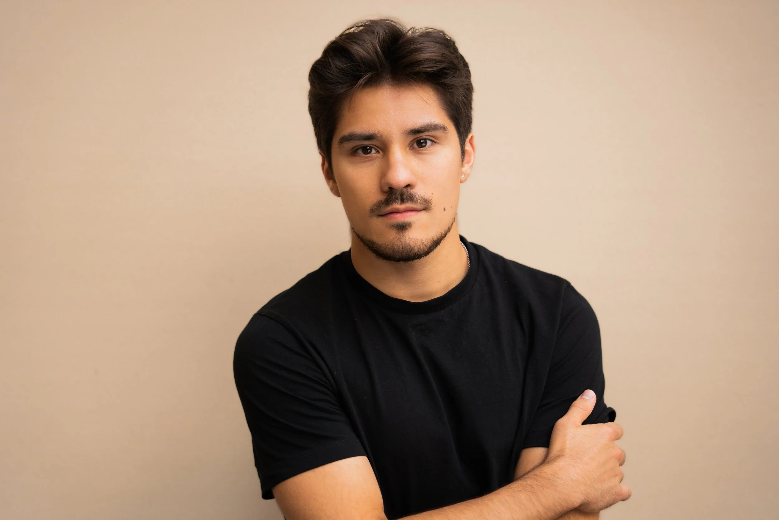 Leo Gonzalez, a young actor with dark brown hair and dark brown eyes, in a black tee shirt against a tan backdrop