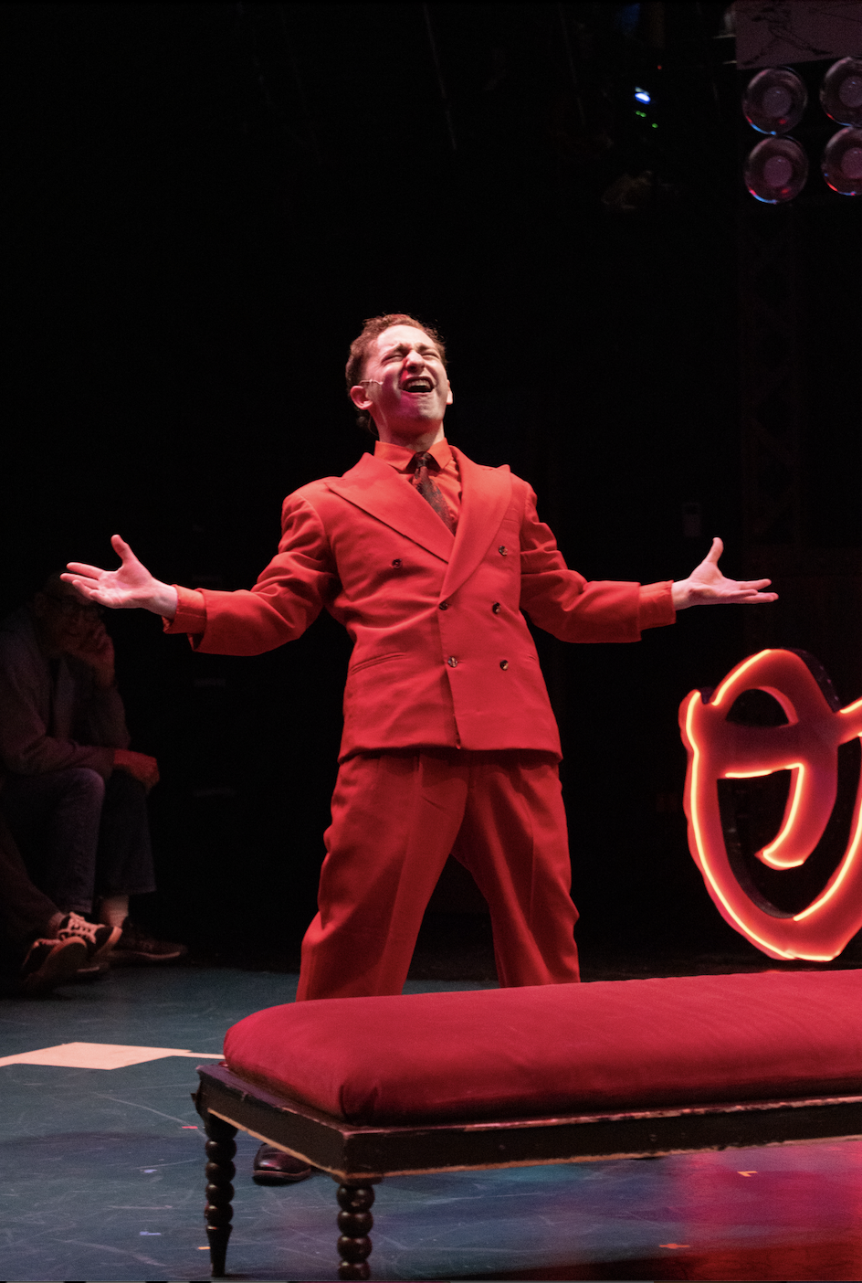 Davey Fried, a young actor in a red suit singing on stage with arms outstretched during NSB's production of Damn Yankees.