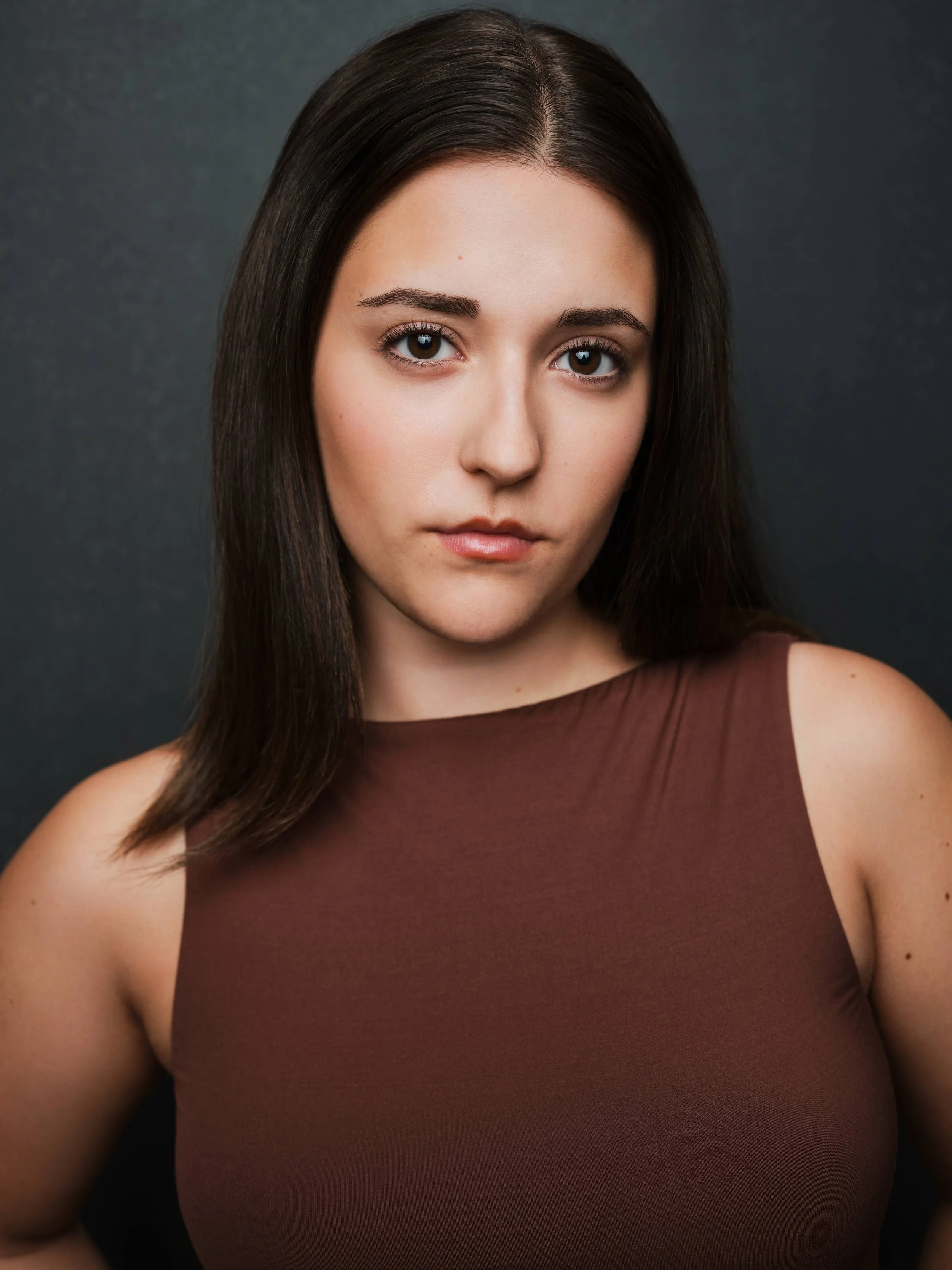 Jessica Schuchardt, a young actress with brown hair and dark brown eyes, in a brown top against a dark gray backdrop