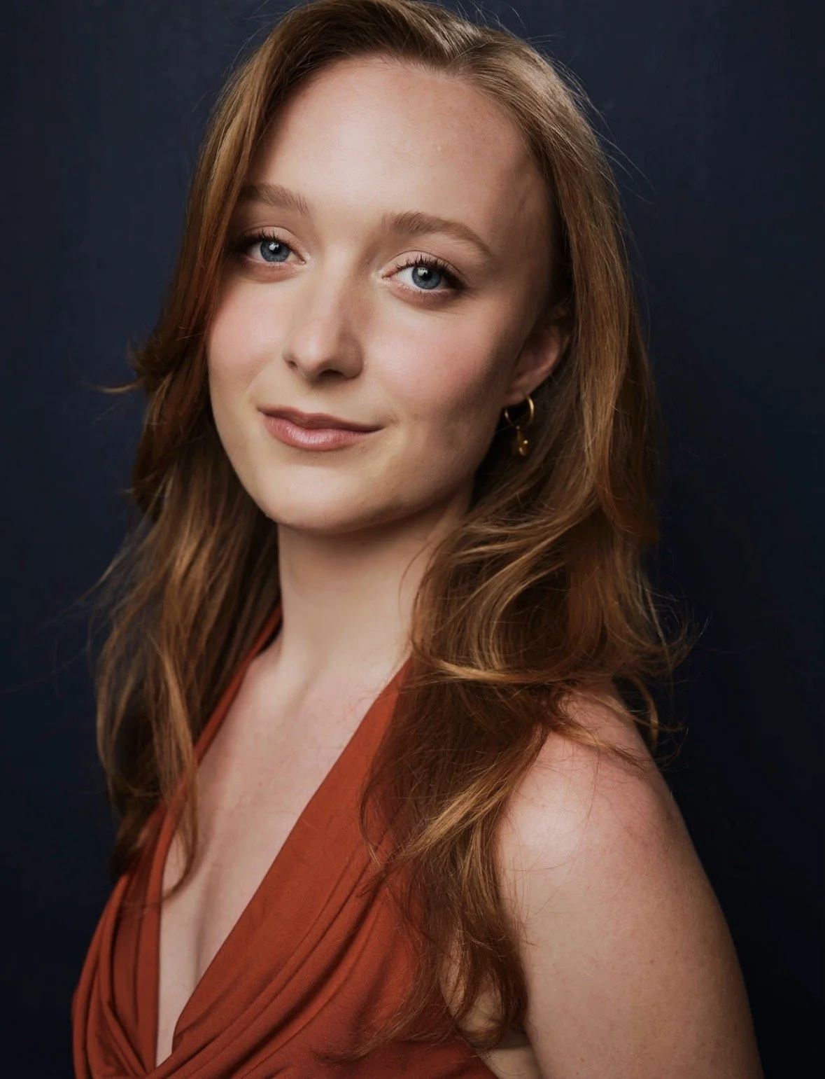 Grace Church, a young actress with red hair and blue eyes wearing a burnt orange top against a navy backdrop