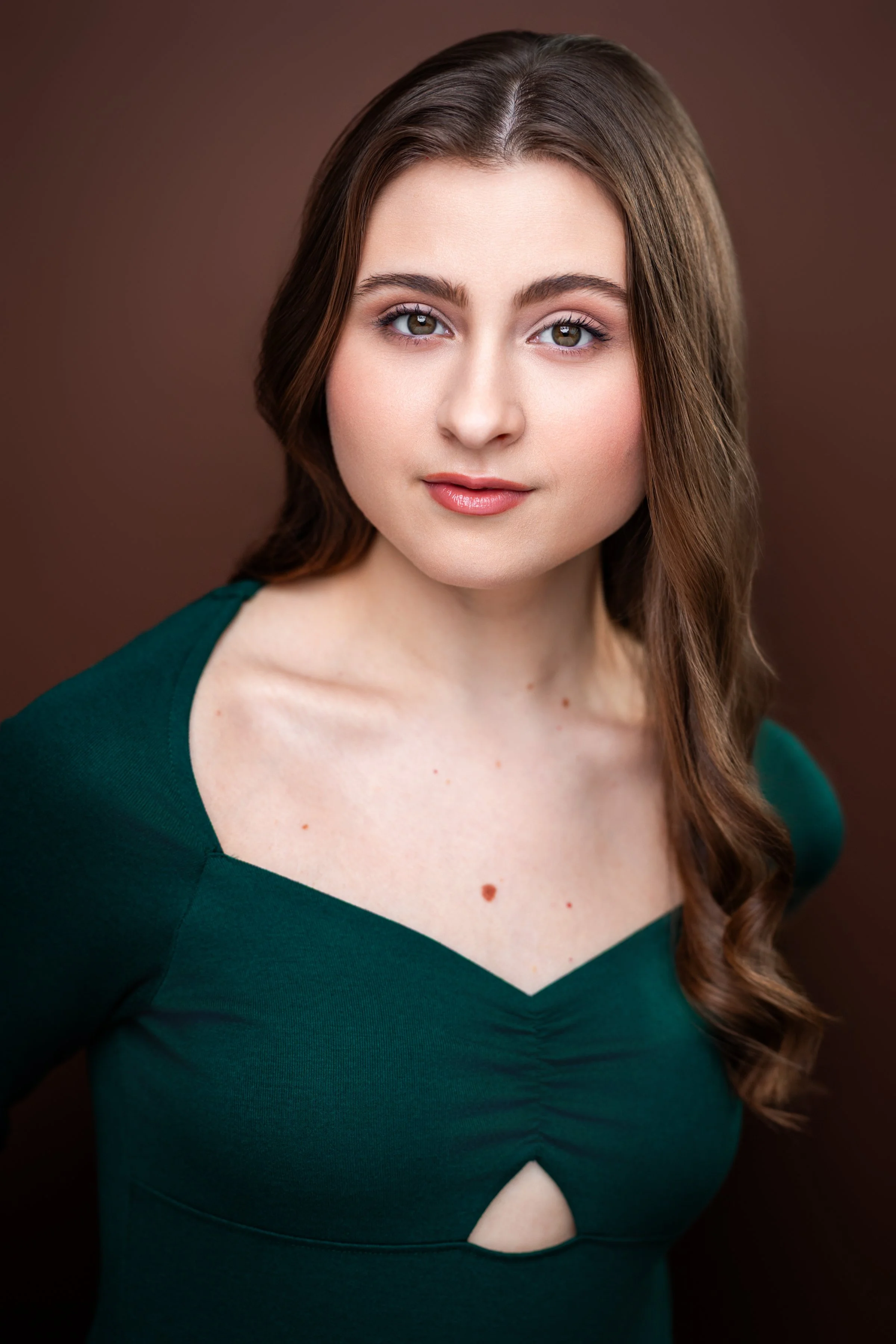 Maria Sablich, a young actress with curled brown hair and brown eyes, in a dark green dress against a brown backdrop