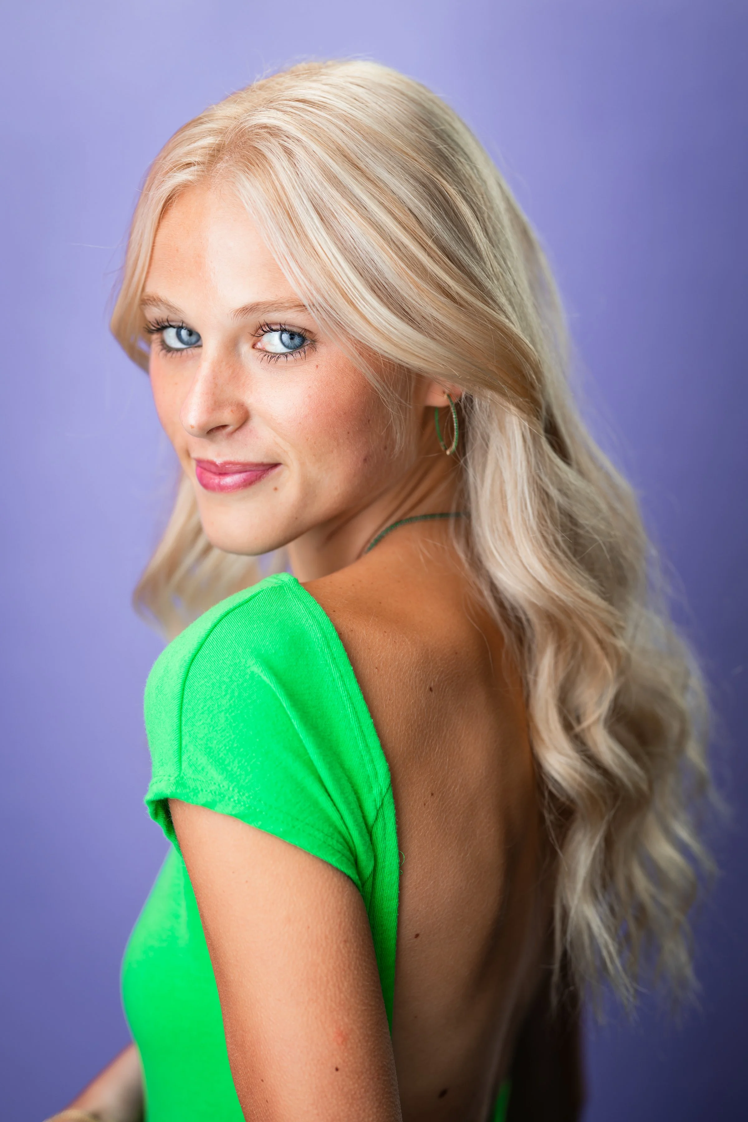 Mia Goldammer, a young actress with wavy light blonde and blue eyes, in a neon green top against a light purple backdrop