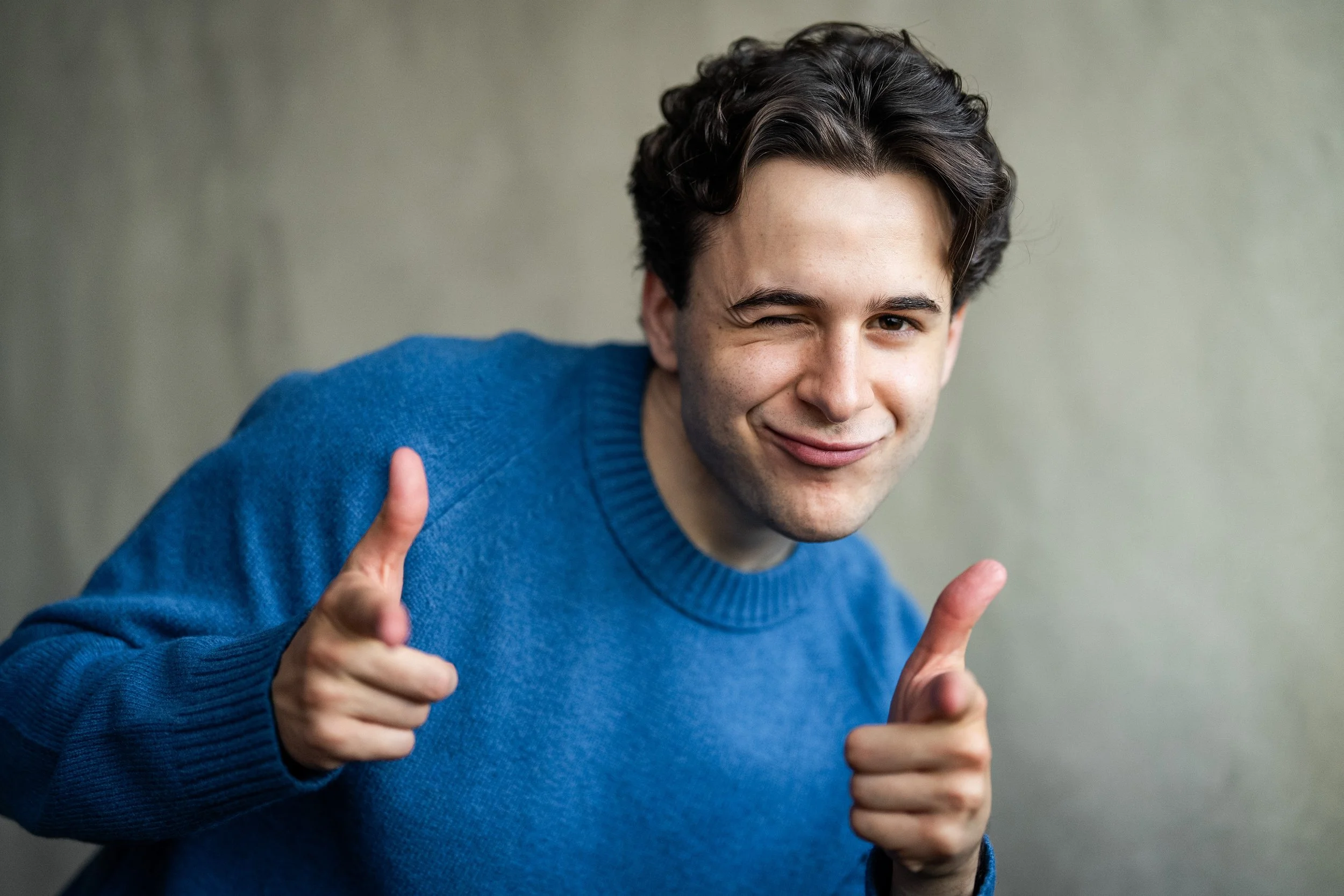 Jeremy DerMovsesian, a young actor with brown hair and brown eyes, in a bright blue sweater pointing and winking at the camera