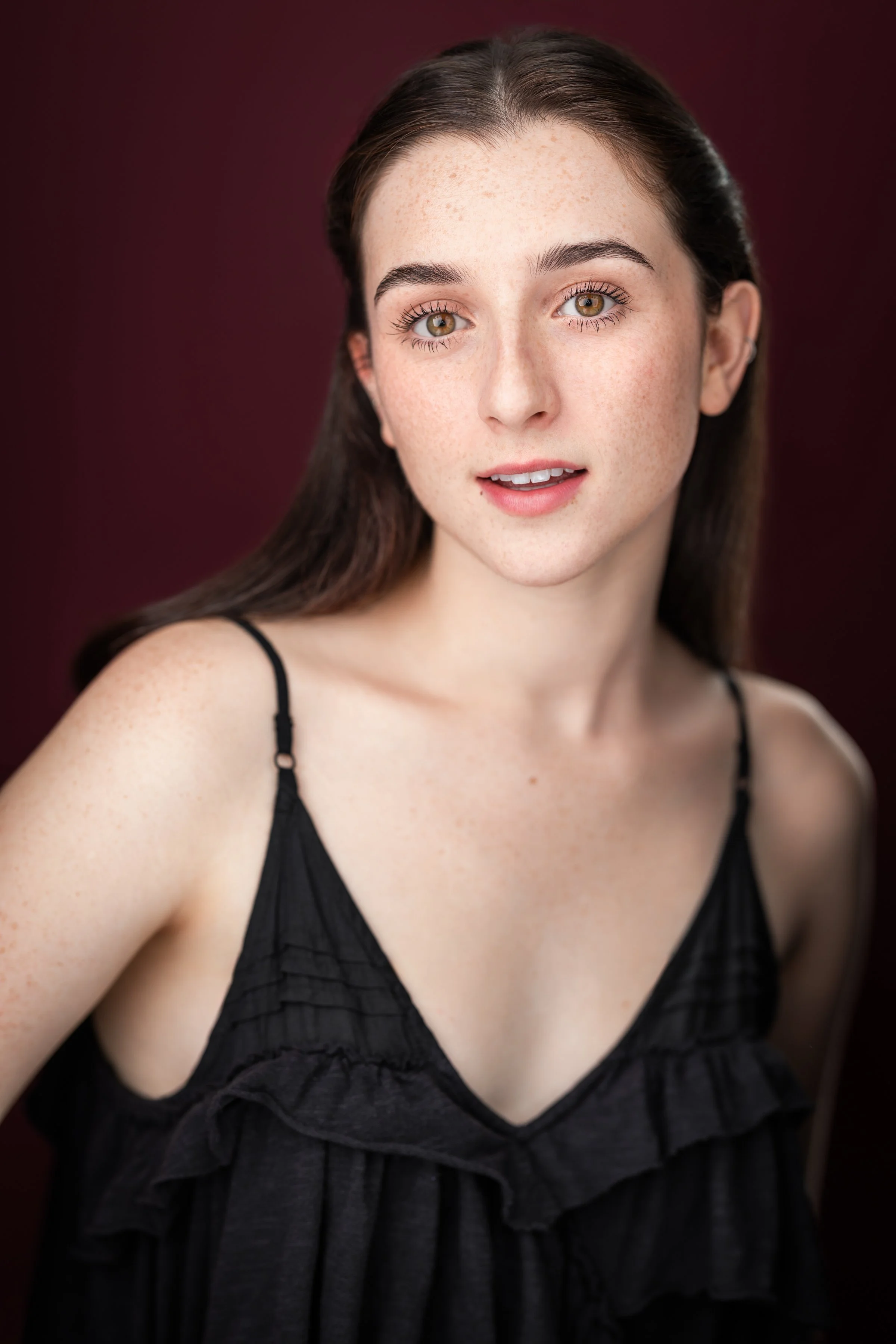 Gemma Strauss, a young actress with brown hair and brown eyes, in a black tank top against a maroon backdrop