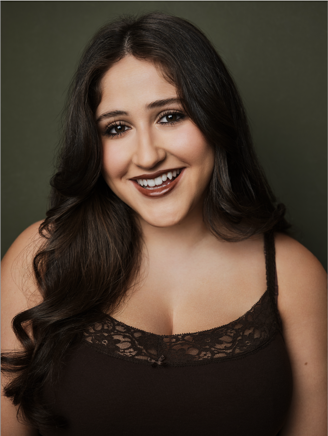 Cece Labowe, a young actress with dark brown hair and dark brown eyes, in a brown tank top with lace against a green backdrop