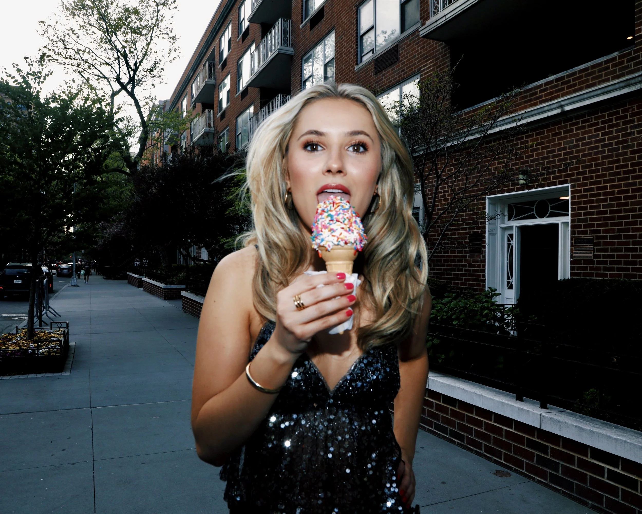Taylor Truckenbrod, a young woman with blonde wavy hair and brown eyes licking an ice cream cone on a New York City street in a sparkly top