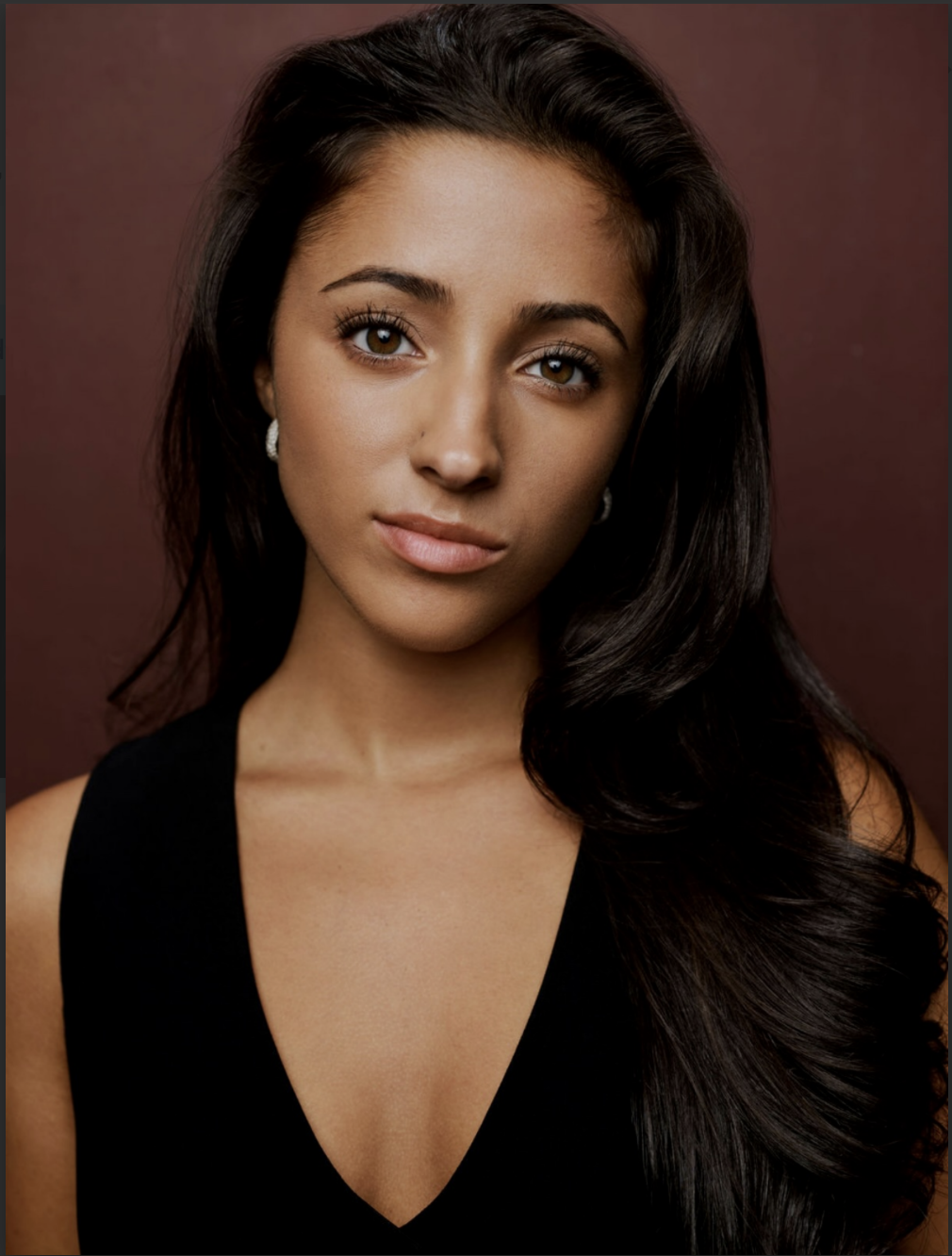 Elana Simard, a young actress with dark brown hair and brown eyes, in a black top against a brown backdrop