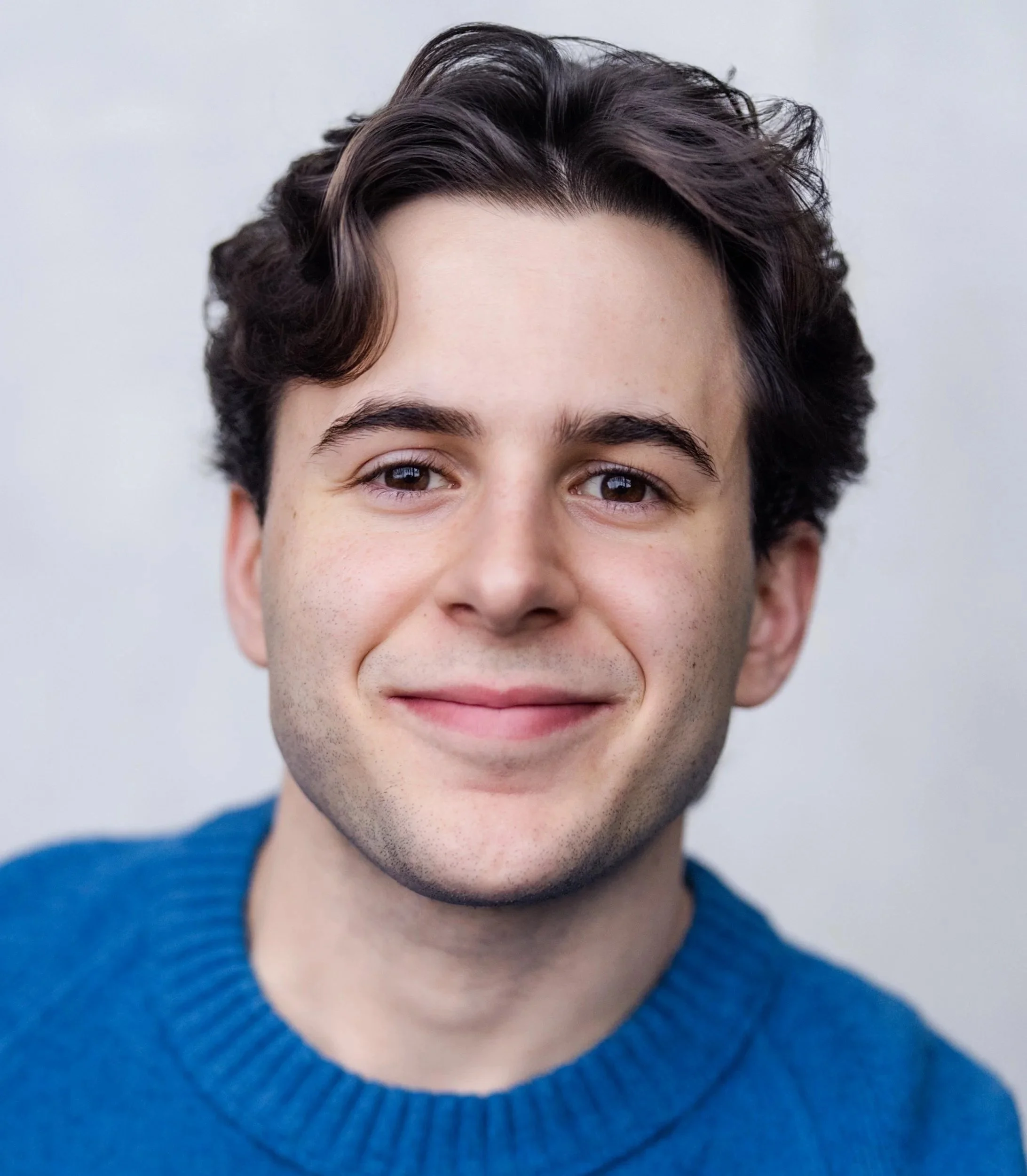 Close-up of Jeremy DerMovsesian, a young actor with dark wavy hair, brown eyes, wearing a blue textured sweater.
