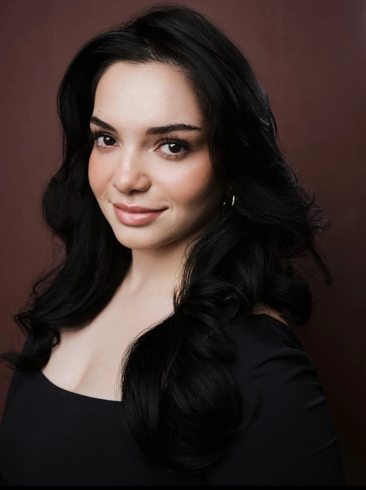 Melina Cruz, a young actress with dark brown hair and dark brown eyes, posing in a black top against a neutral backdrop