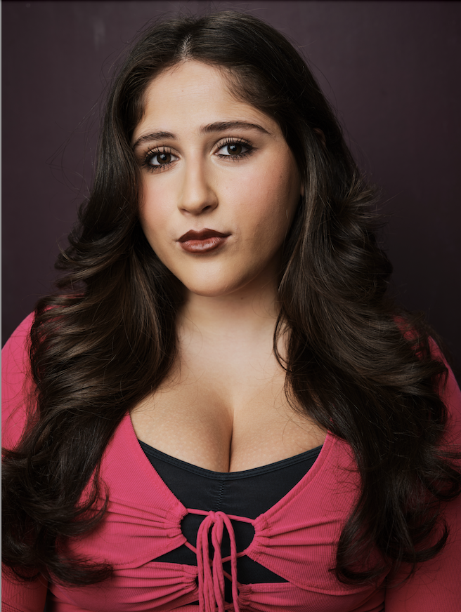 Cece Labowe, a young actress with dark brown hair and dark brown eyes, in a hot pink and black layered top against a neutral backdrop