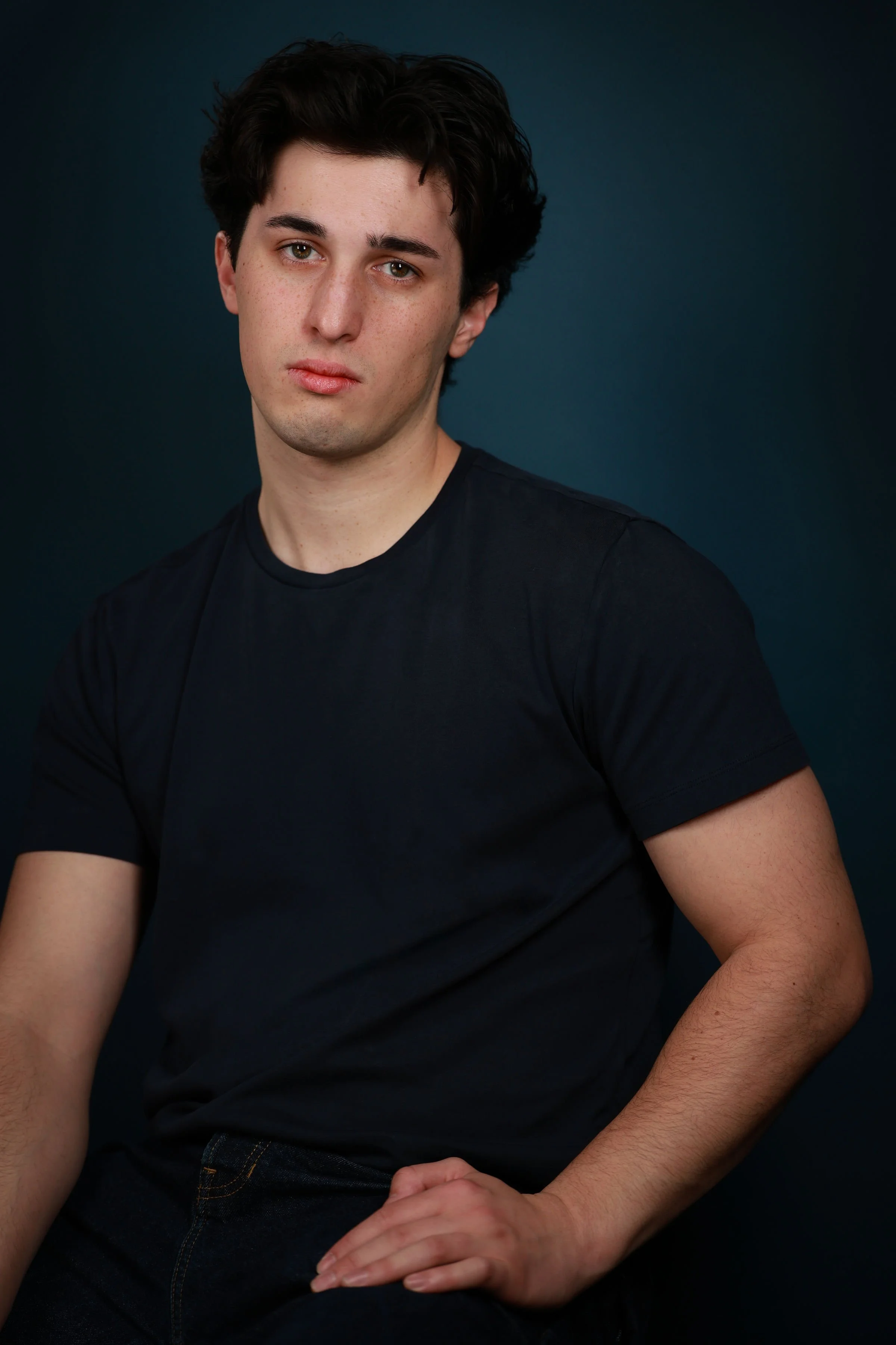 Miguel Castillo, a young actor with dark brown hair and brown eyes, wearing a black tee shirt against a dark turquoise backdrop