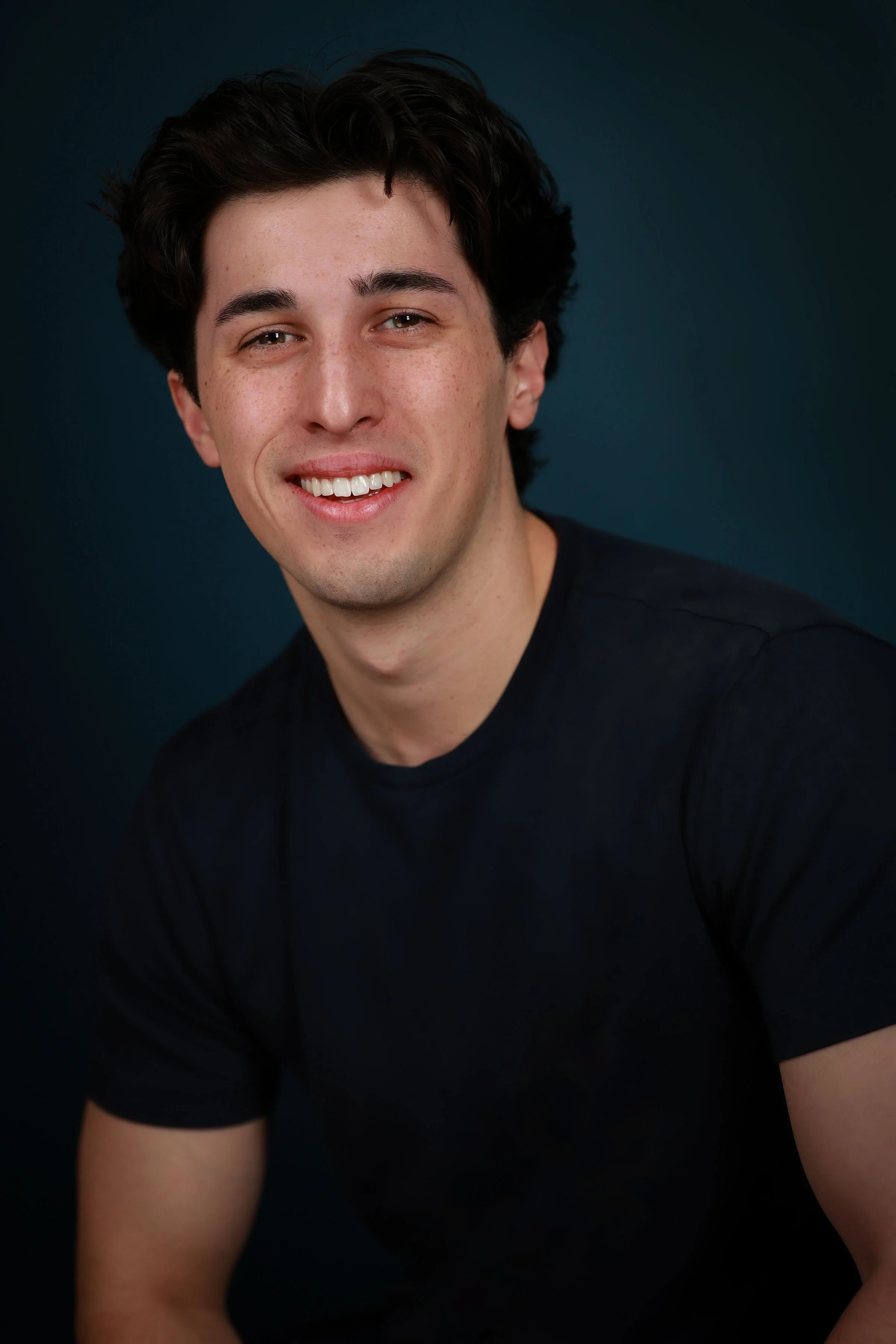 Miguel Castillo, a young actor with dark brown hair and brown eyes, in a black shirt against a dark turquoise backdrop